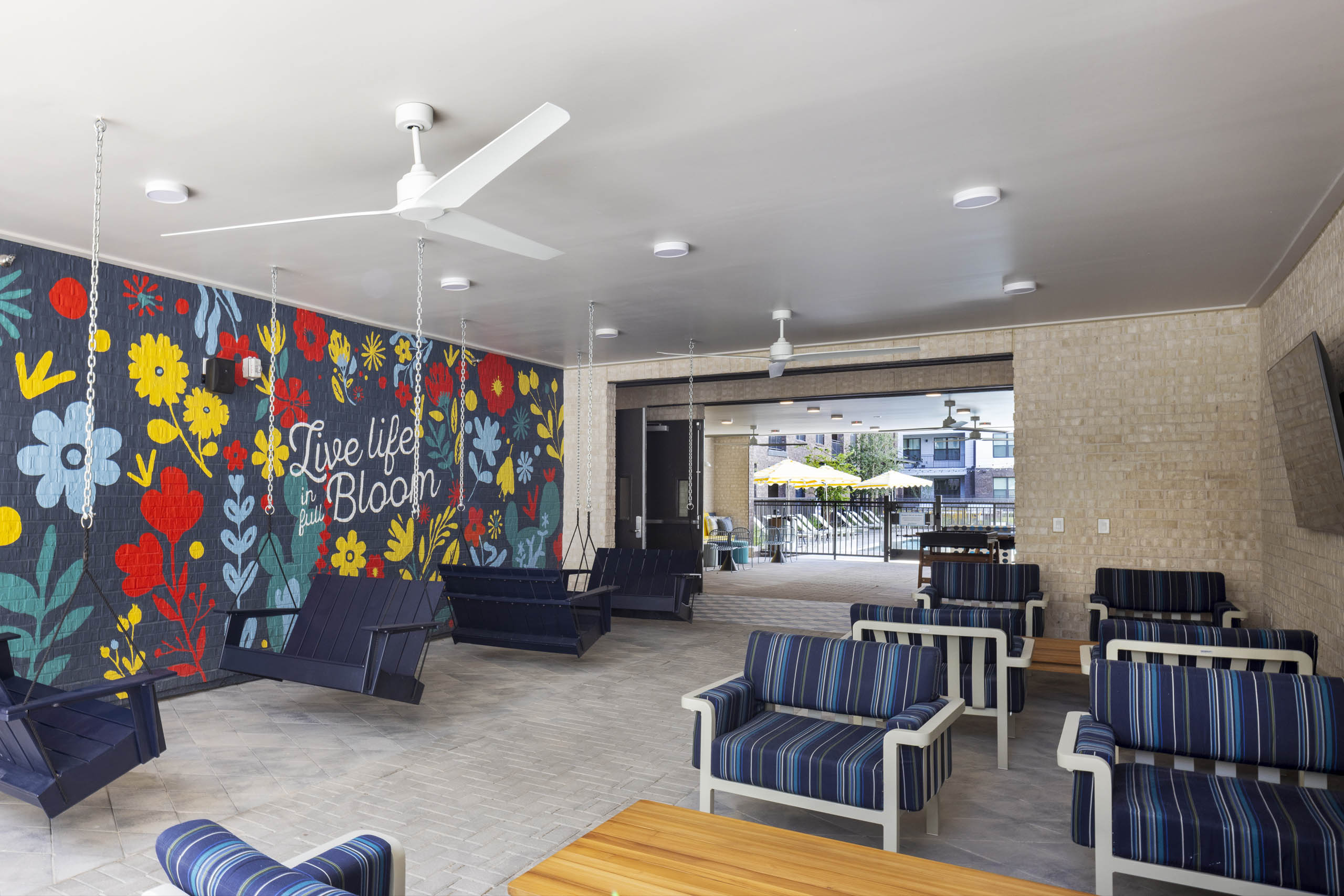 Covered patio at AMLI North Park apartment community with cushioned chairs hanging swings flower mural ceiling fans and view of courtyard
