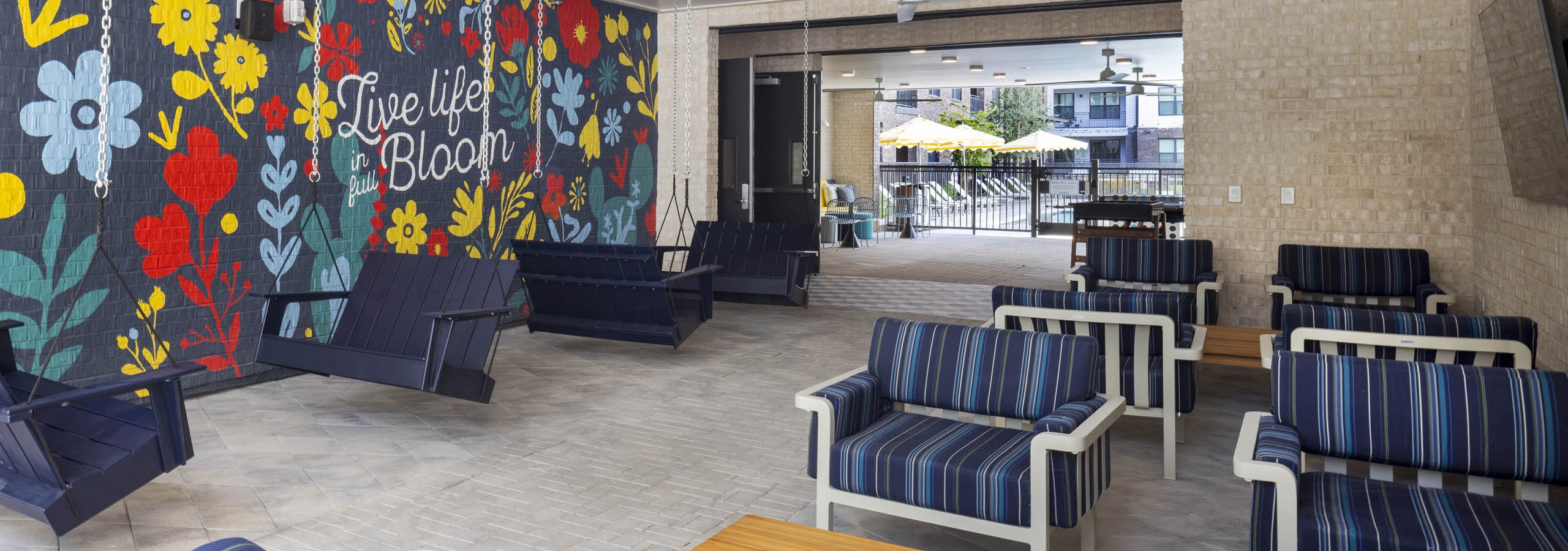 Covered patio at AMLI North Park apartment community with cushioned chairs hanging swings flower mural ceiling fans and view of courtyard