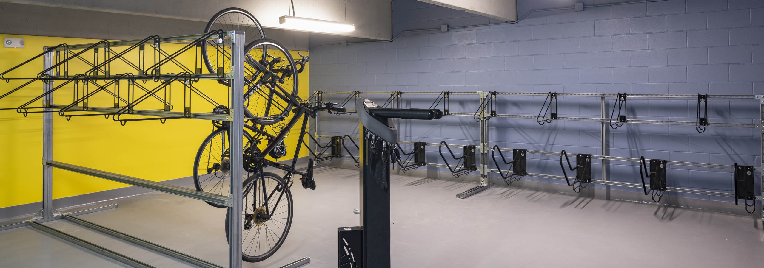 Bike room at AMLI North Park with yellow and blue walls metal racks on both sides and several bikes hanging vertically