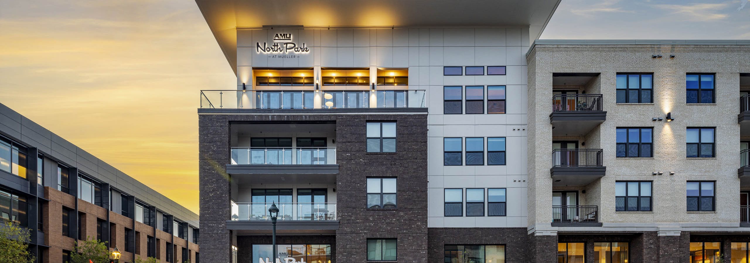 Corner view of AMLI North Park apartment building with balconies large windows stop sign trees and sunset sky