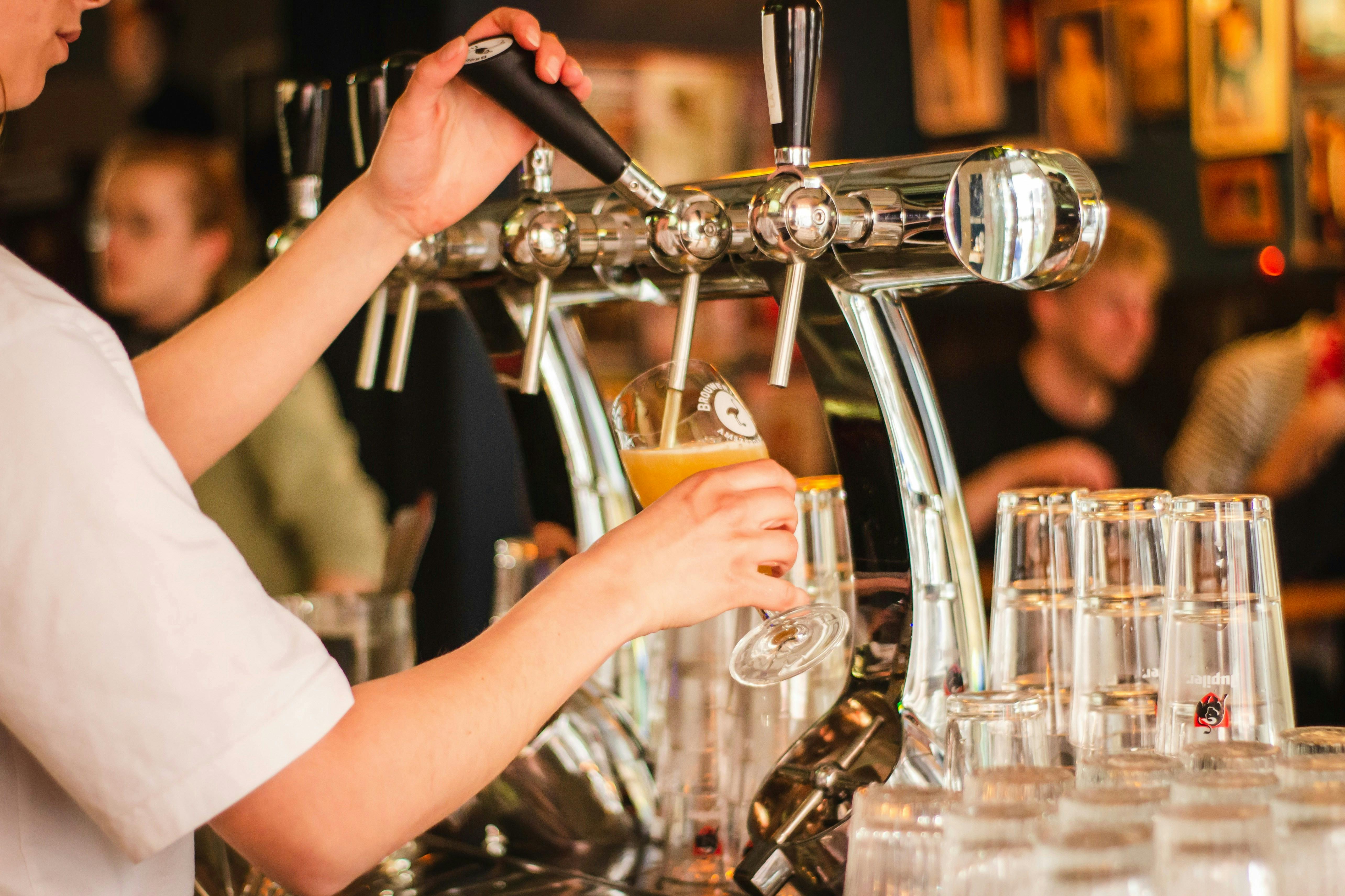 A bartender is pulling a beer tap handle to fill a pint glass. A row of empty glasses is in the foreground.
