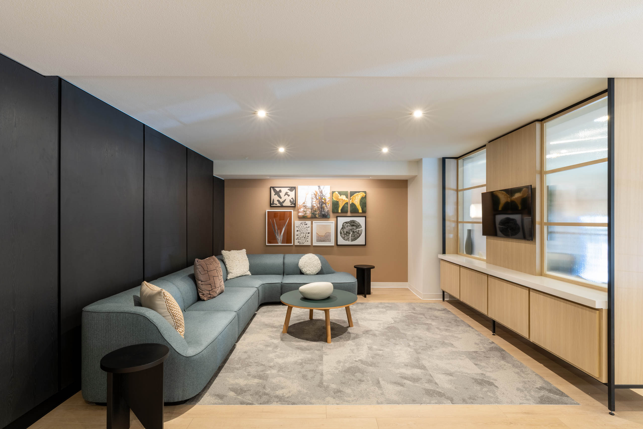 Interior view of AMLI 535 apartments lounge with curved blue sofa, round coffee table, art wall, TV, and modern black paneling.