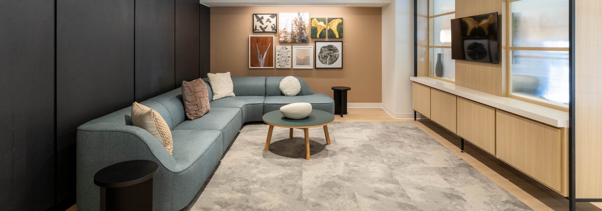 Interior view of AMLI 535 apartments lounge with curved blue sofa, round coffee table, art wall, TV, and modern black paneling.