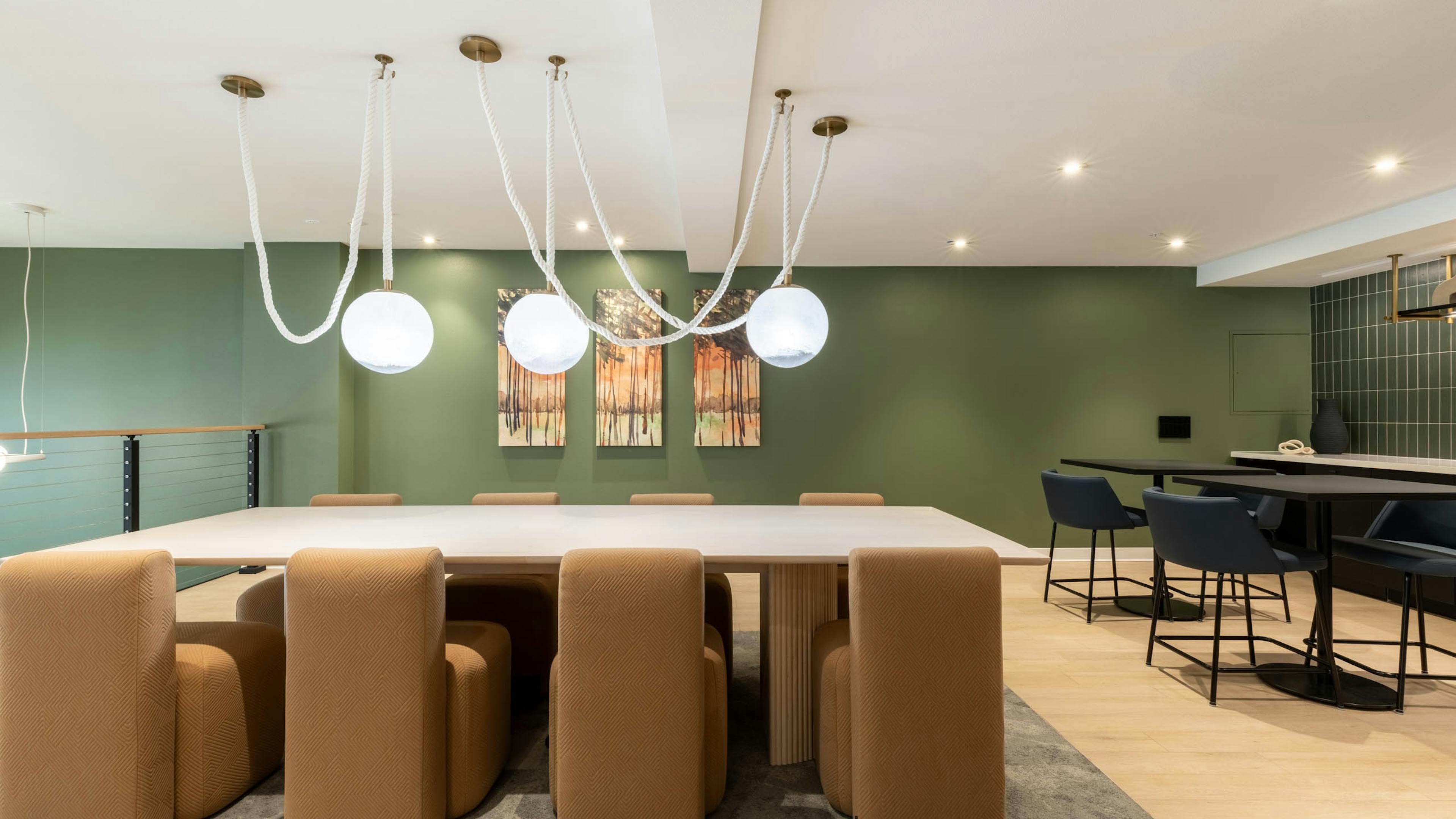 Wide view of AMLI 535 apartments dining lounge with light wood table, brown upholstered chairs, green accent wall, and pendant lights.