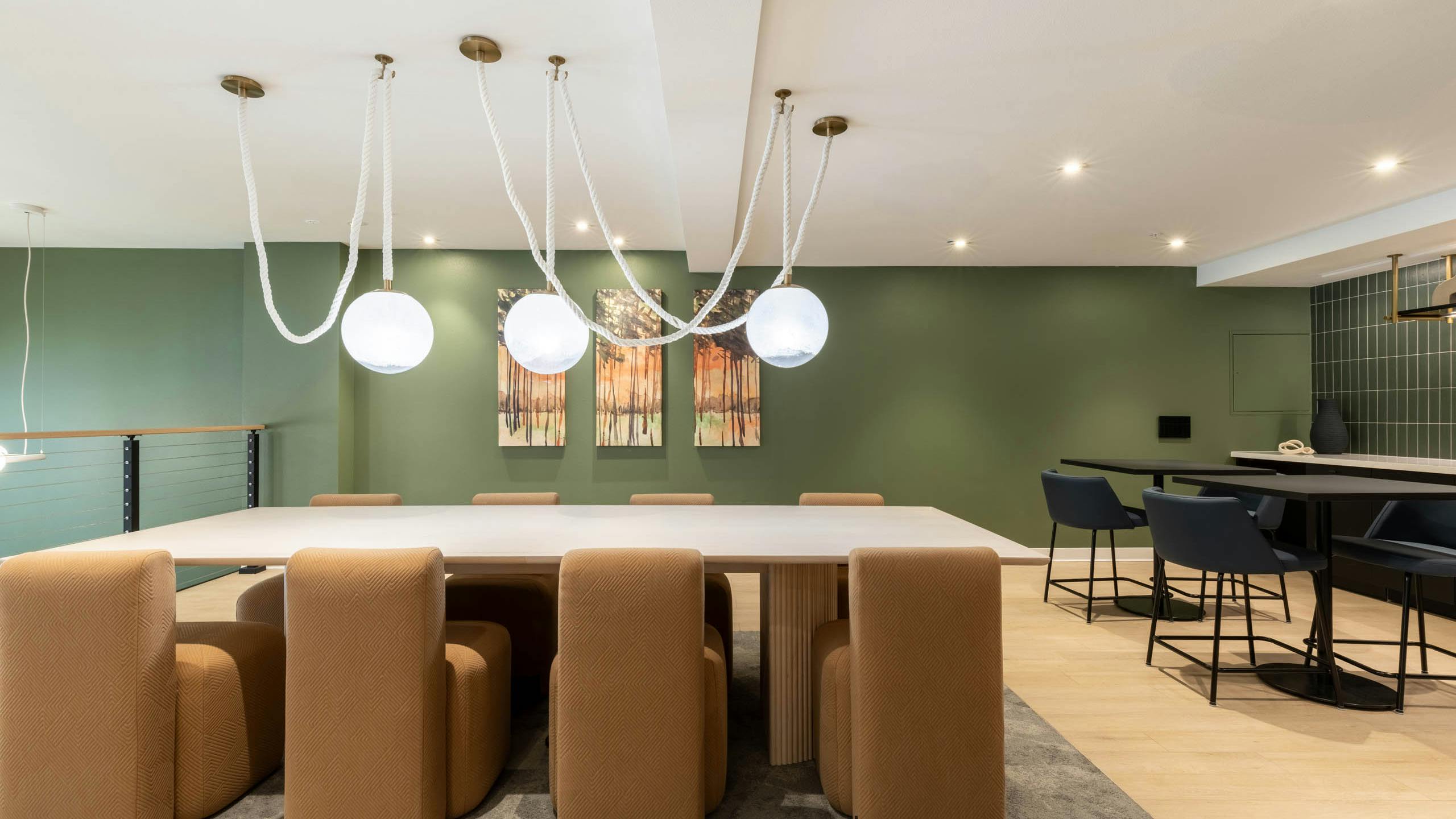 Wide view of AMLI 535 apartments dining lounge with light wood table, brown upholstered chairs, green accent wall, and pendant lights.