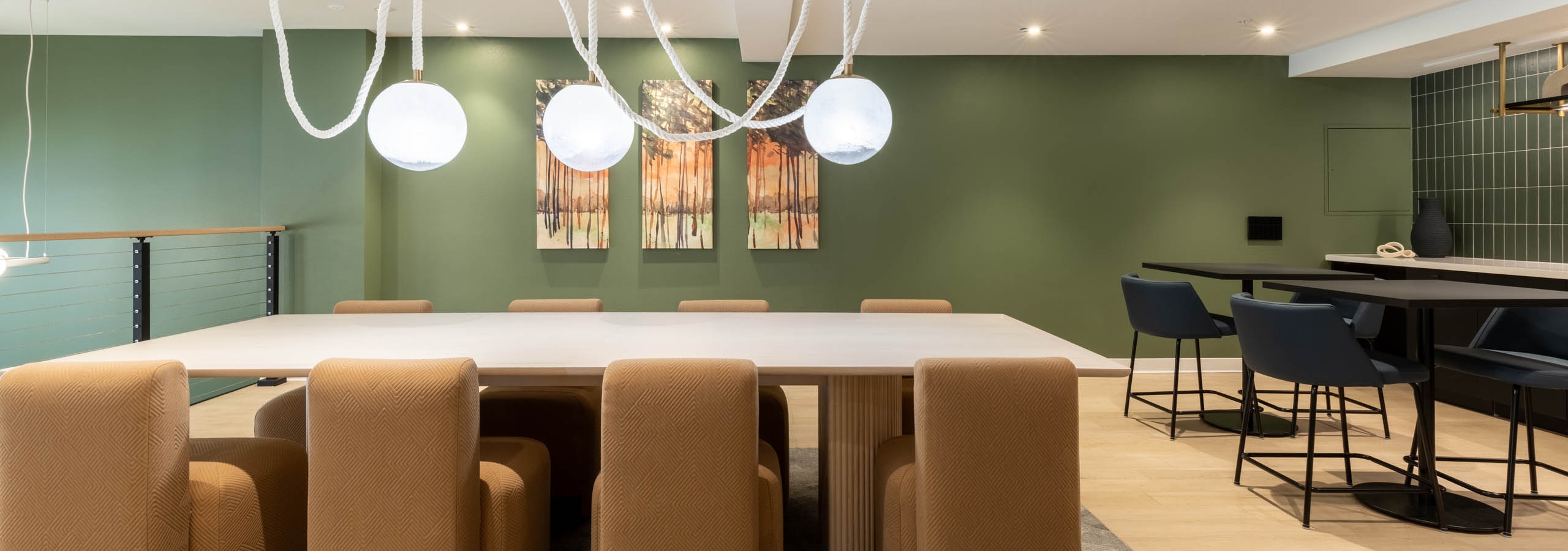 Wide view of AMLI 535 apartments dining lounge with light wood table, brown upholstered chairs, green accent wall, and pendant lights.