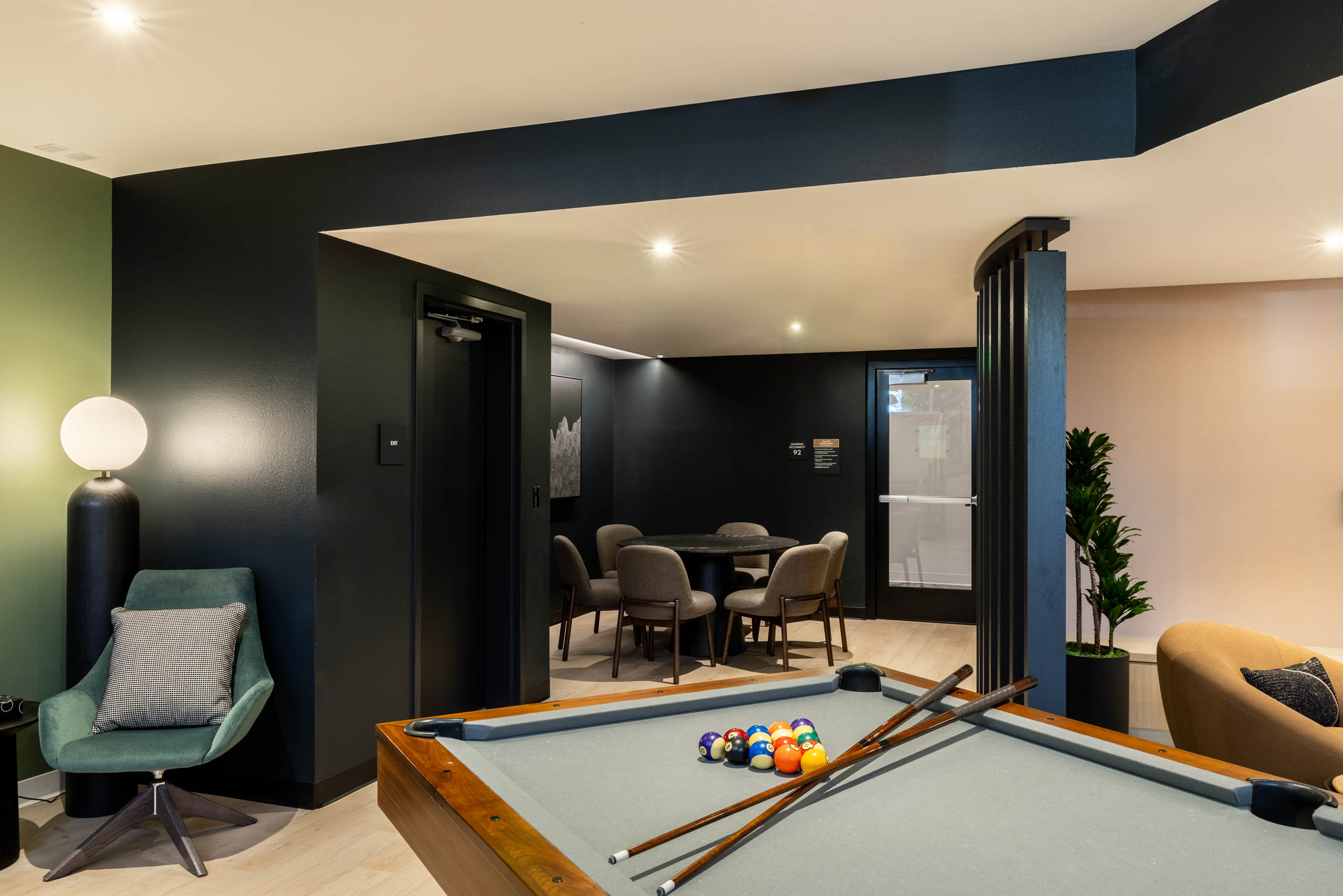 View of AMLI 535 apartments gaming nook with pool table, cue sticks, plush green chair, and poker table surrounded by black walls.