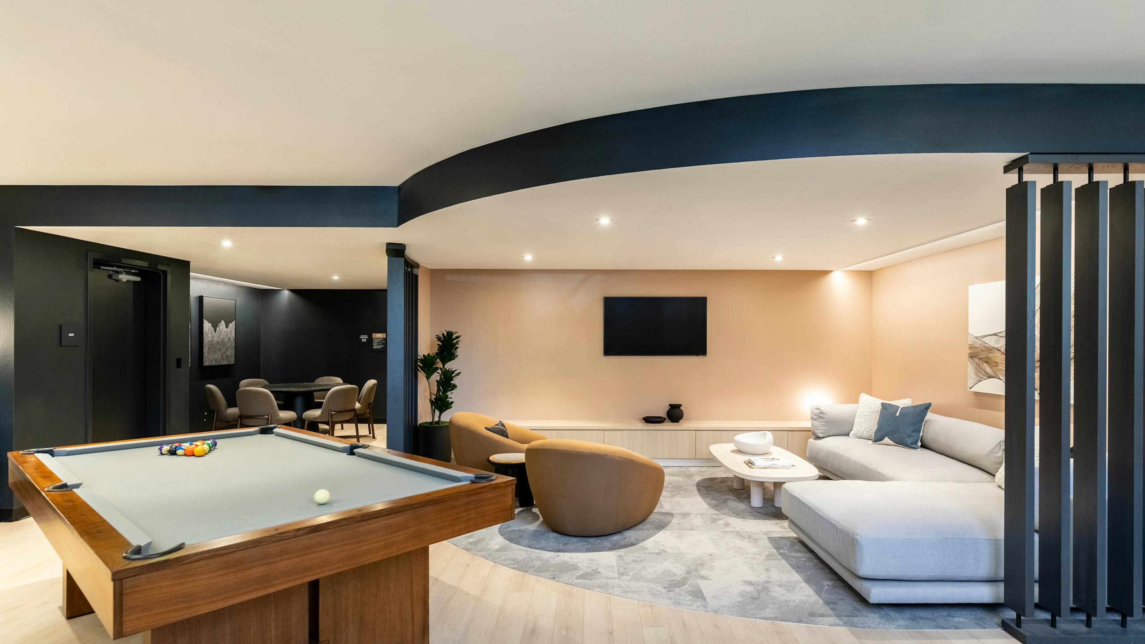 Game lounge at AMLI 535 apartments with billiards table, TV, tan armchairs, sectional sofa, and a soft beige and black color scheme.