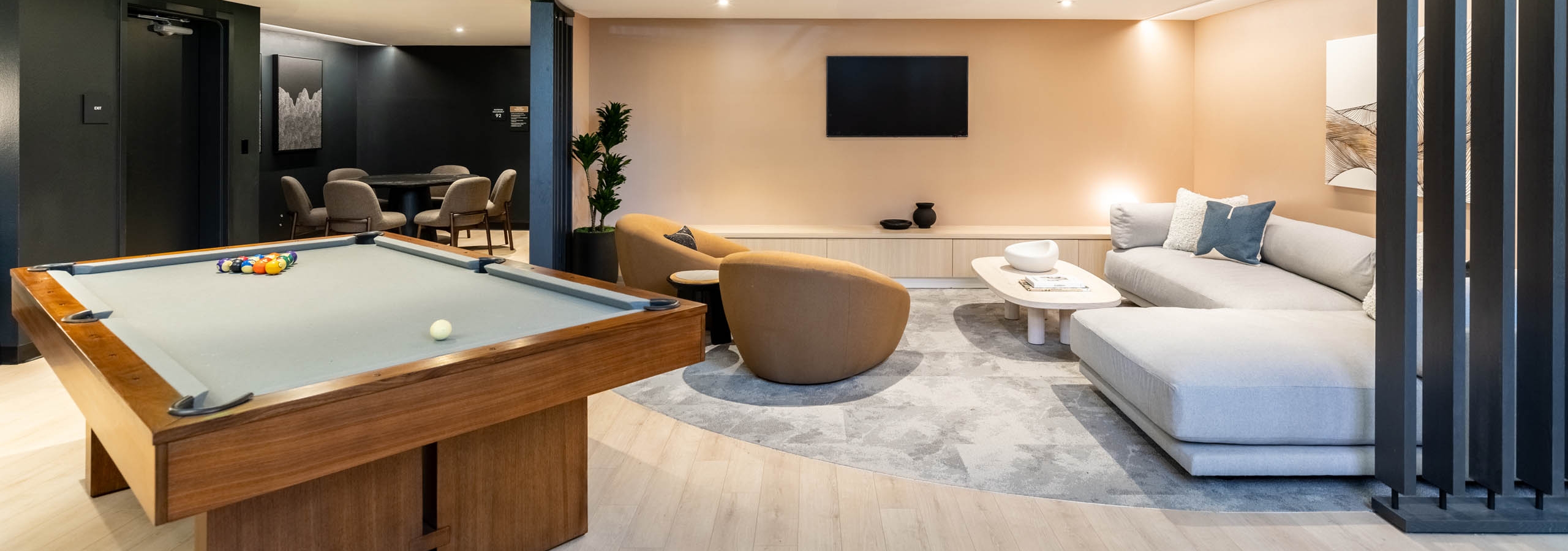 Game lounge at AMLI 535 apartments with billiards table, TV, tan armchairs, sectional sofa, and a soft beige and black color scheme.