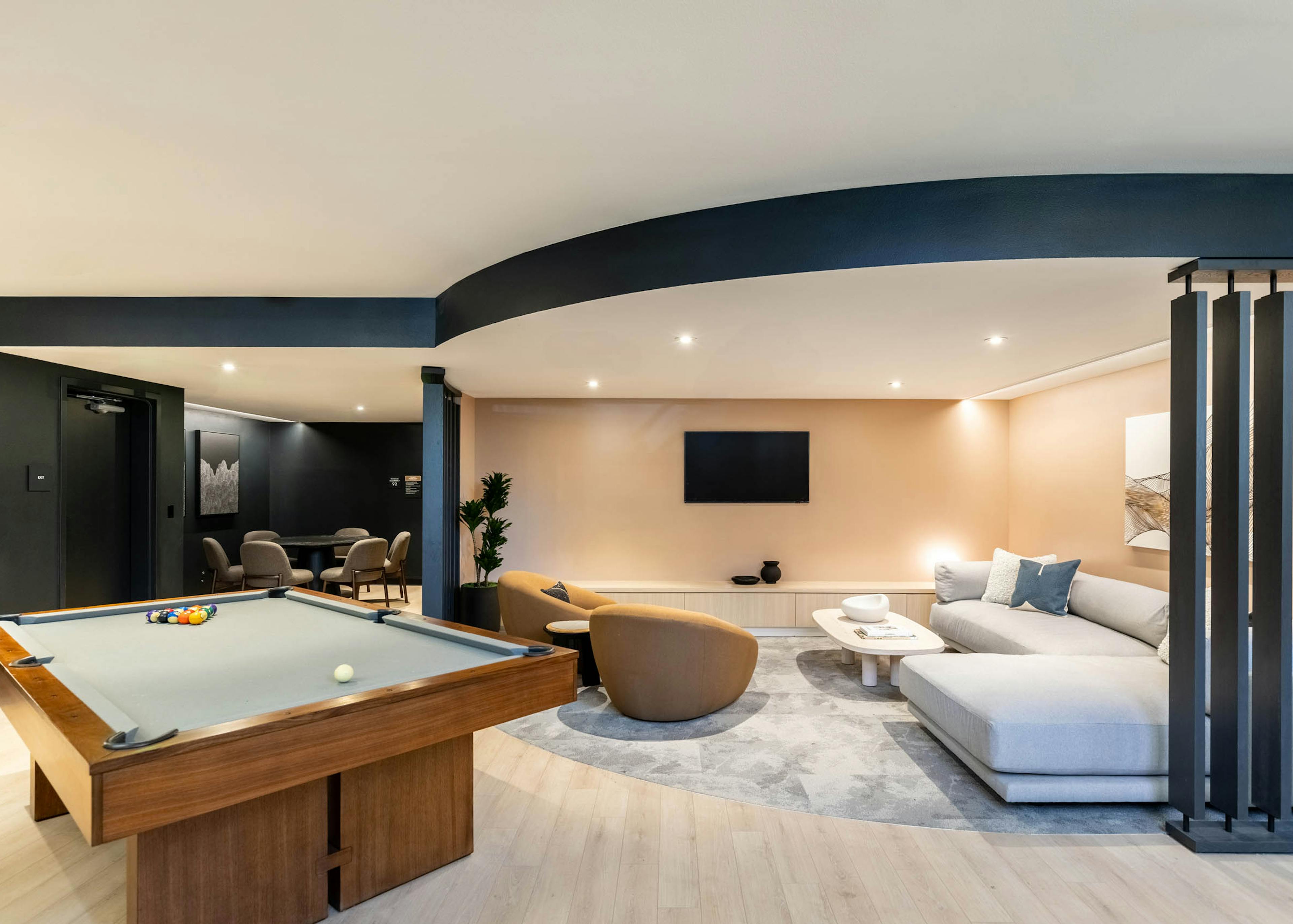 Game lounge at AMLI 535 apartments with billiards table, TV, tan armchairs, sectional sofa, and a soft beige and black color scheme.