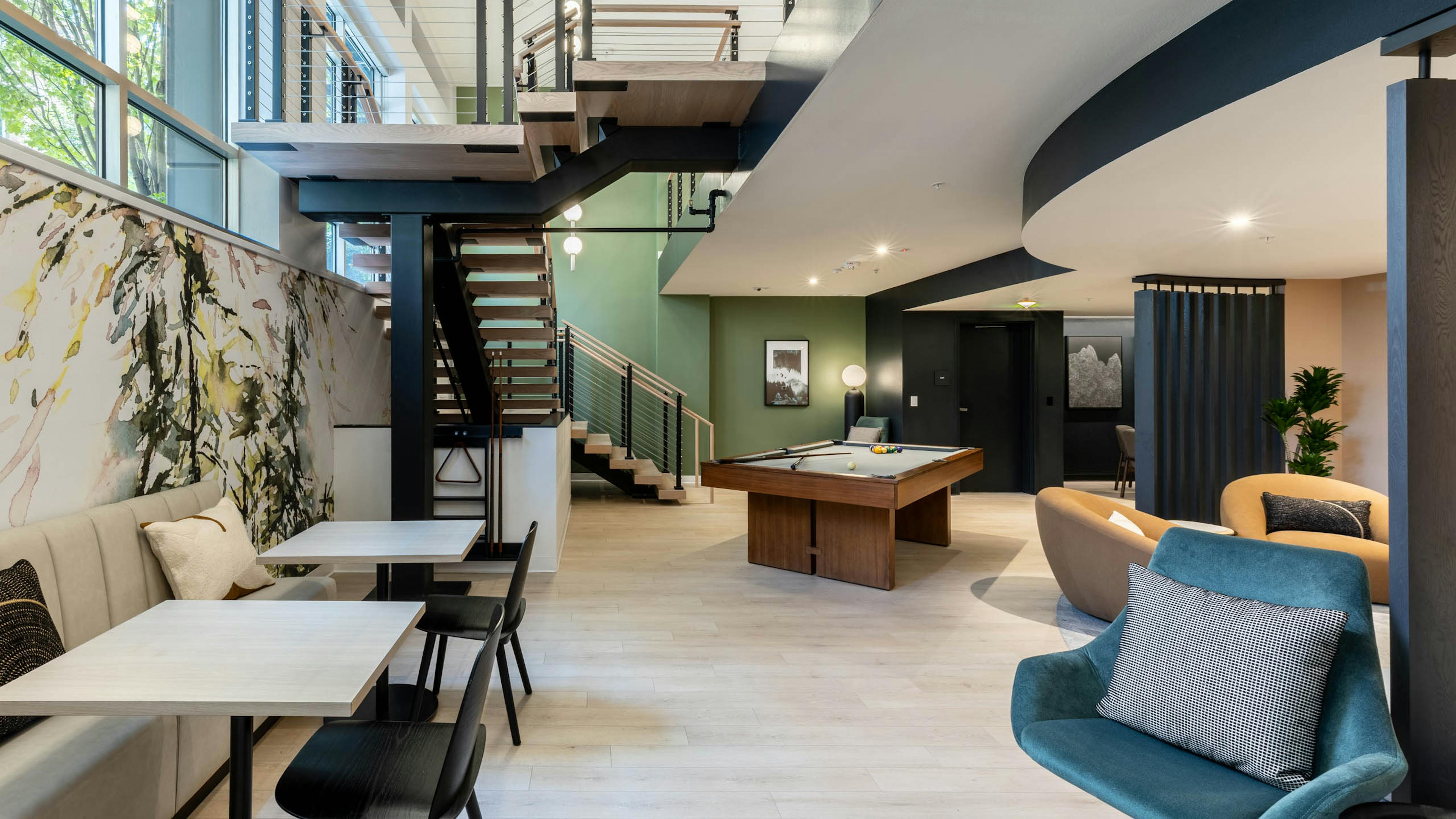 Open lounge at AMLI 535 apartments with large staircase, pool table, modern lighting, green accent wall, and booth seating area.