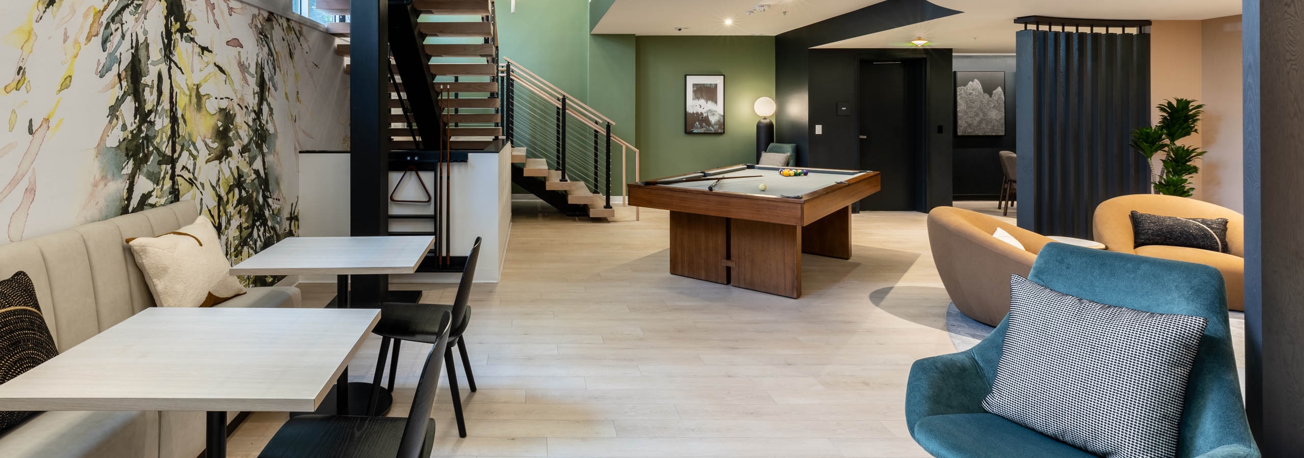 Open lounge at AMLI 535 apartments with large staircase, pool table, modern lighting, green accent wall, and booth seating area.