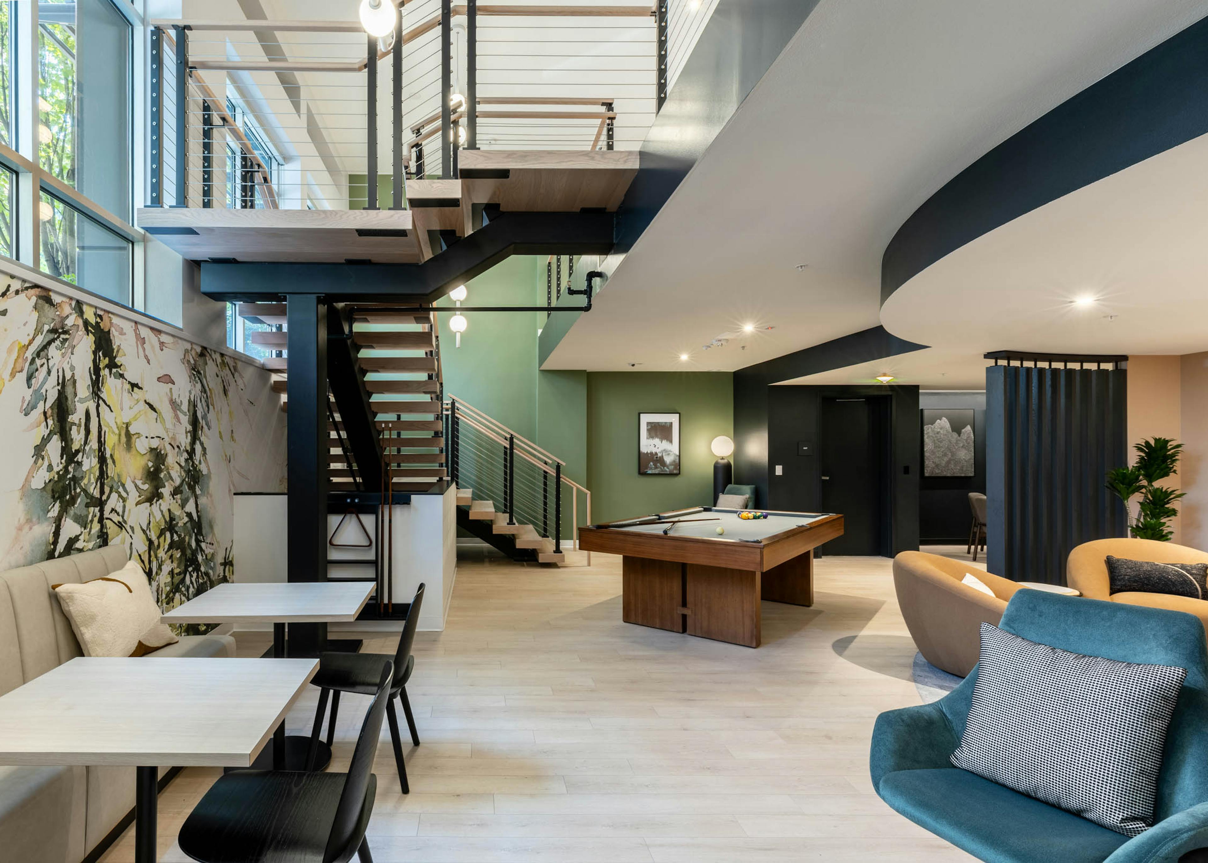 Open lounge at AMLI 535 apartments with large staircase, pool table, modern lighting, green accent wall, and booth seating area.