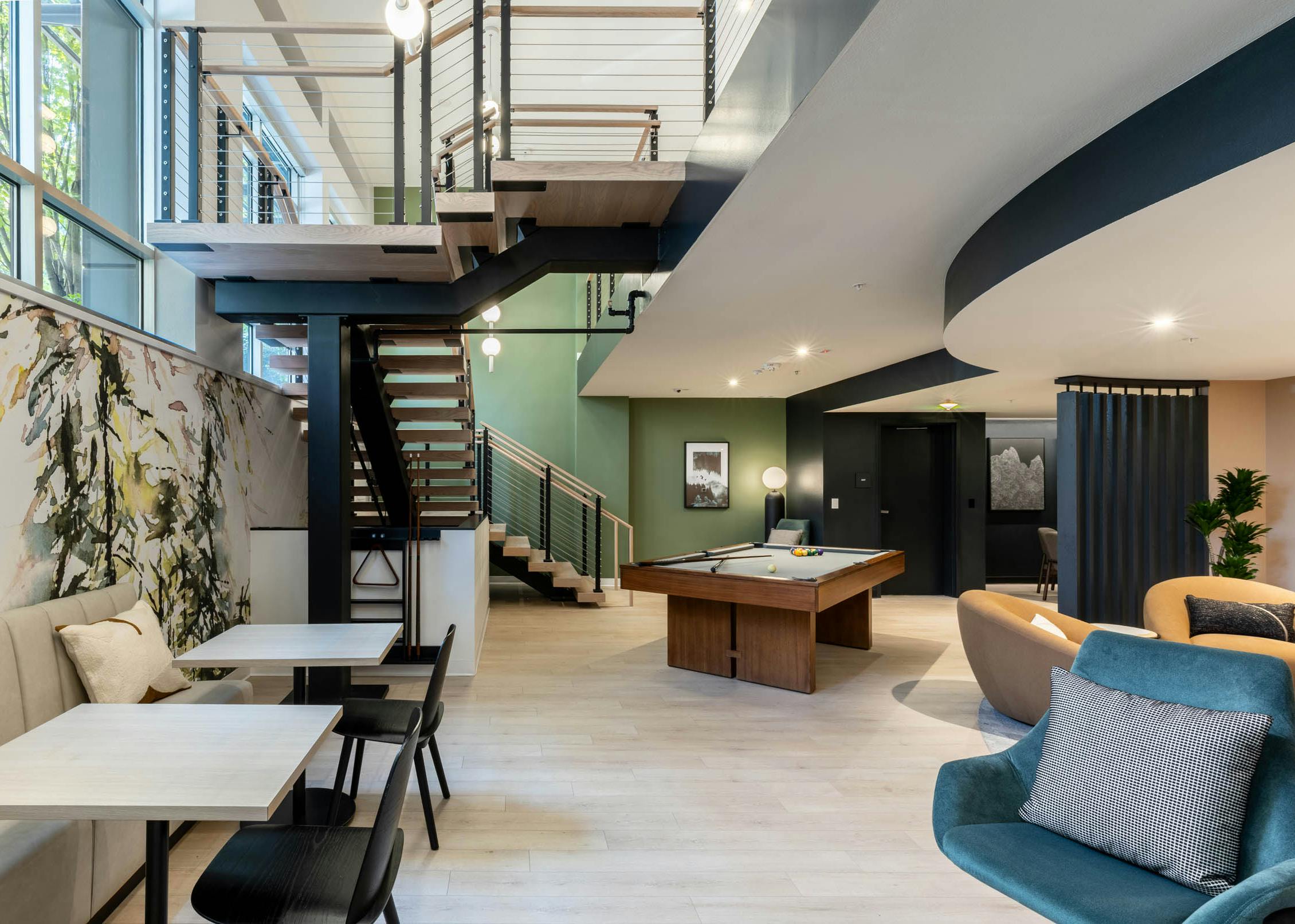 Open lounge at AMLI 535 apartments with large staircase, pool table, modern lighting, green accent wall, and booth seating area.