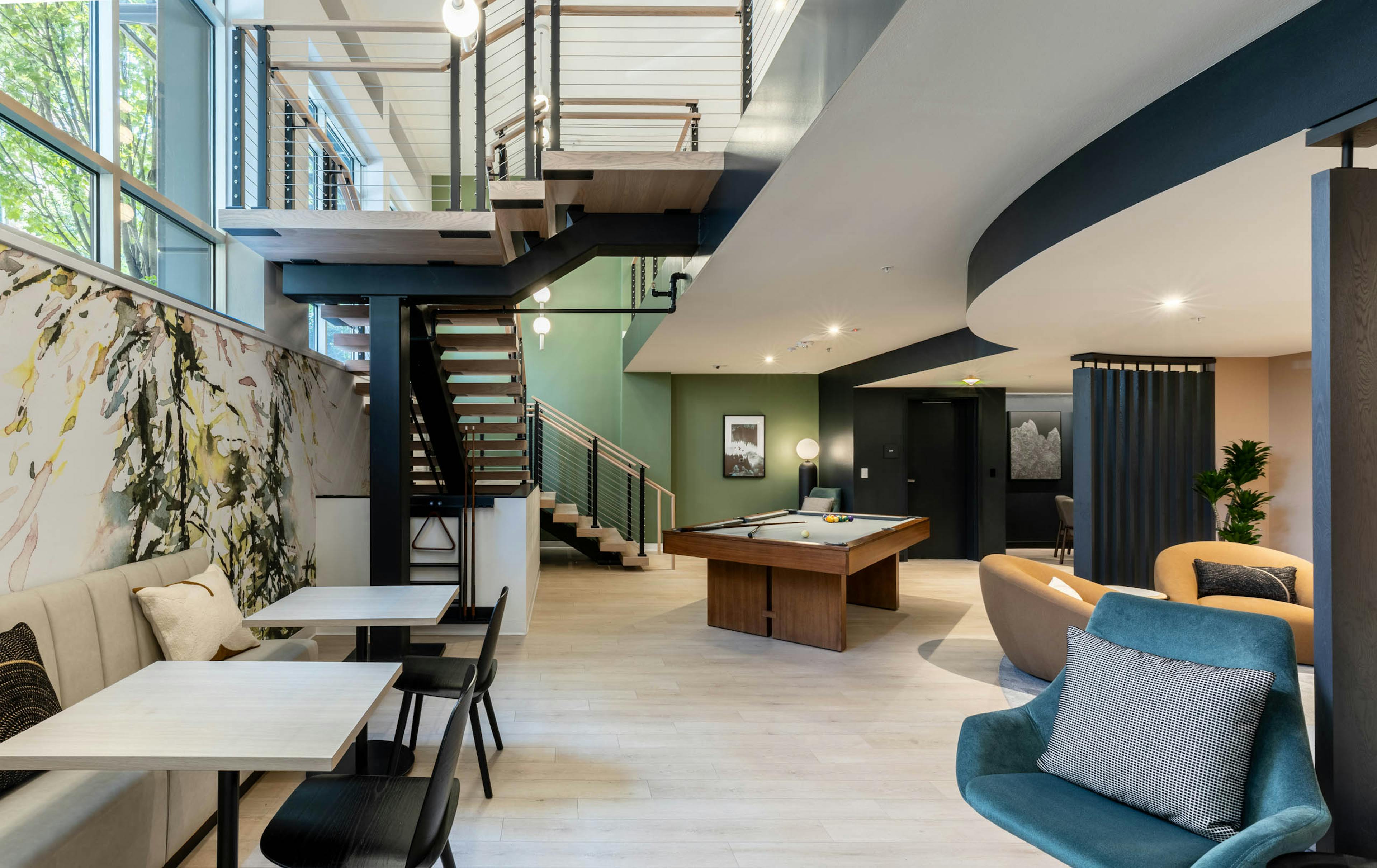 Open lounge at AMLI 535 apartments with large staircase, pool table, modern lighting, green accent wall, and booth seating area.