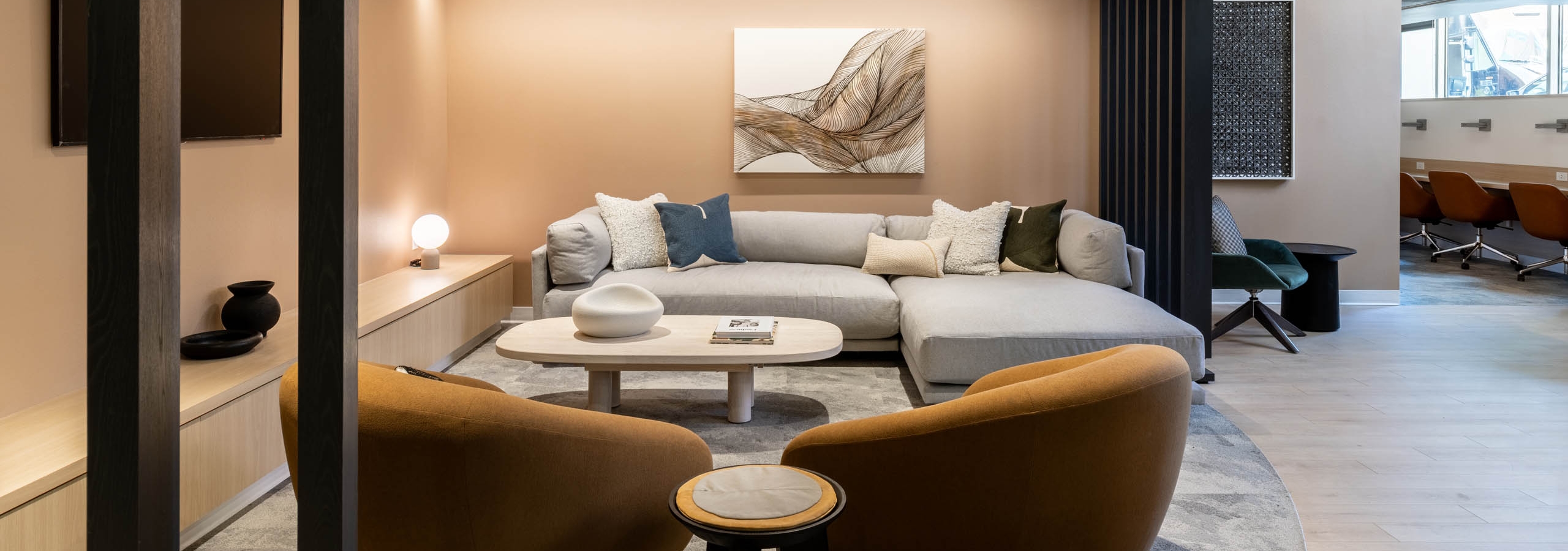 Cozy corner lounge at AMLI 535 apartments with plush light gray sectional, tan coffee table, brown accent chairs, and wall-mounted TV.