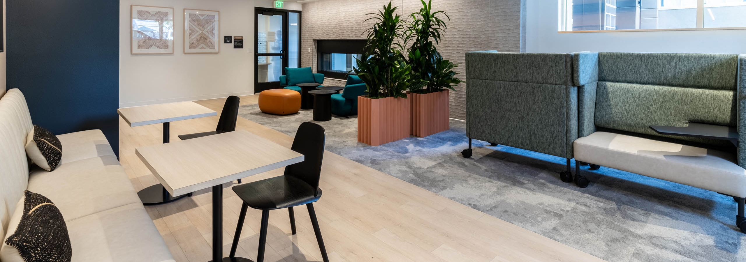 Community lounge at AMLI 535 apartments with booth and table seating, lounge chairs, potted plants, and a contemporary fireplace.