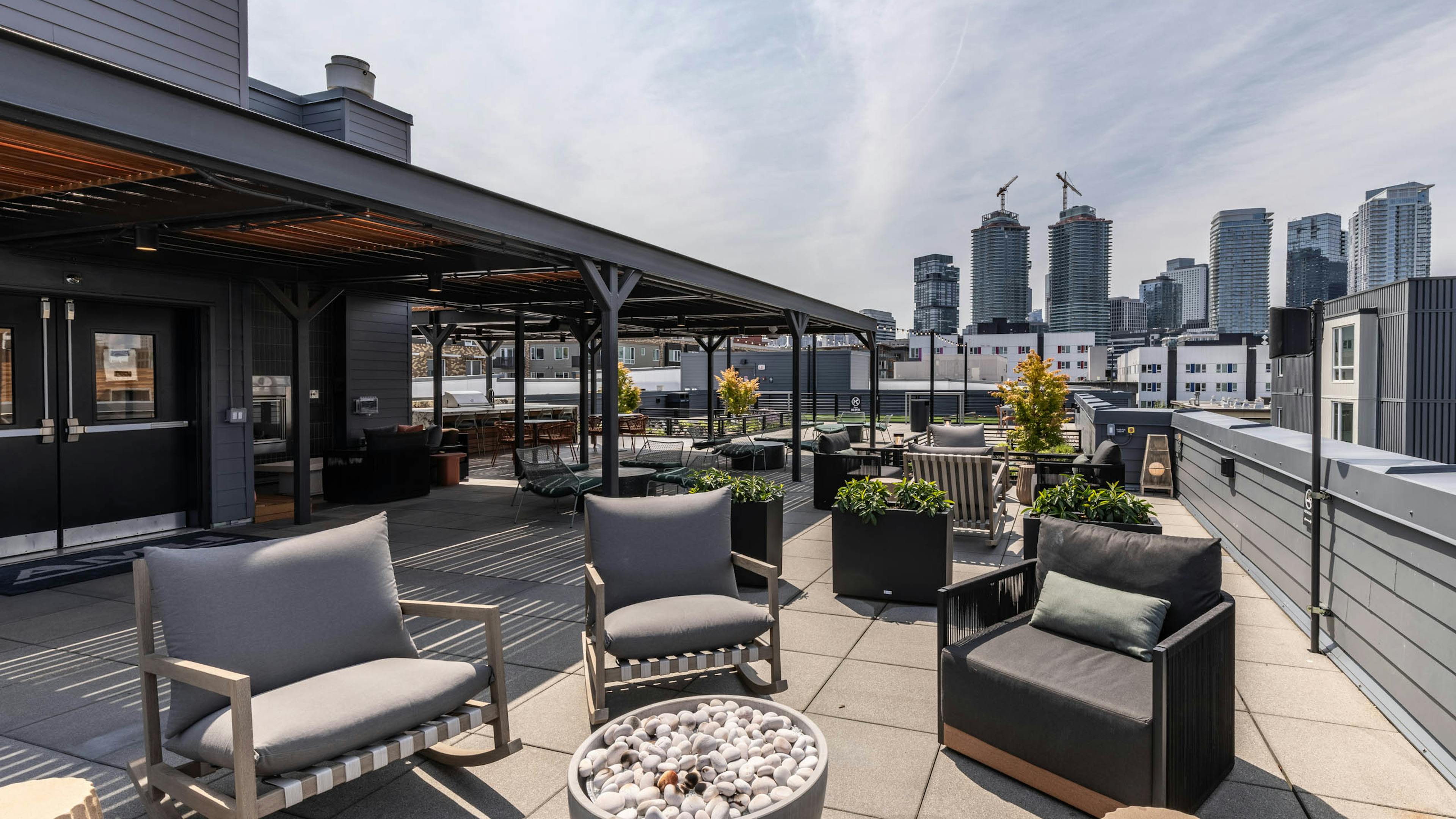 Rooftop lounge with cushioned chairs, fire pit, skyline views, and covered seating under black pergola at AMLI 535 apartments.
