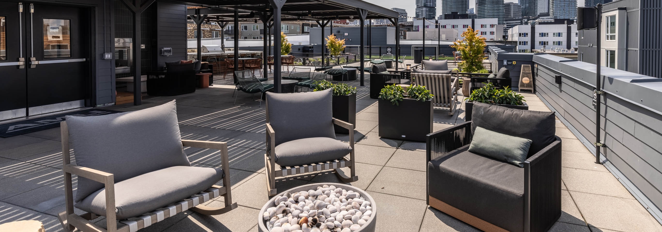 Rooftop lounge with cushioned chairs, fire pit, skyline views, and covered seating under black pergola at AMLI 535 apartments.