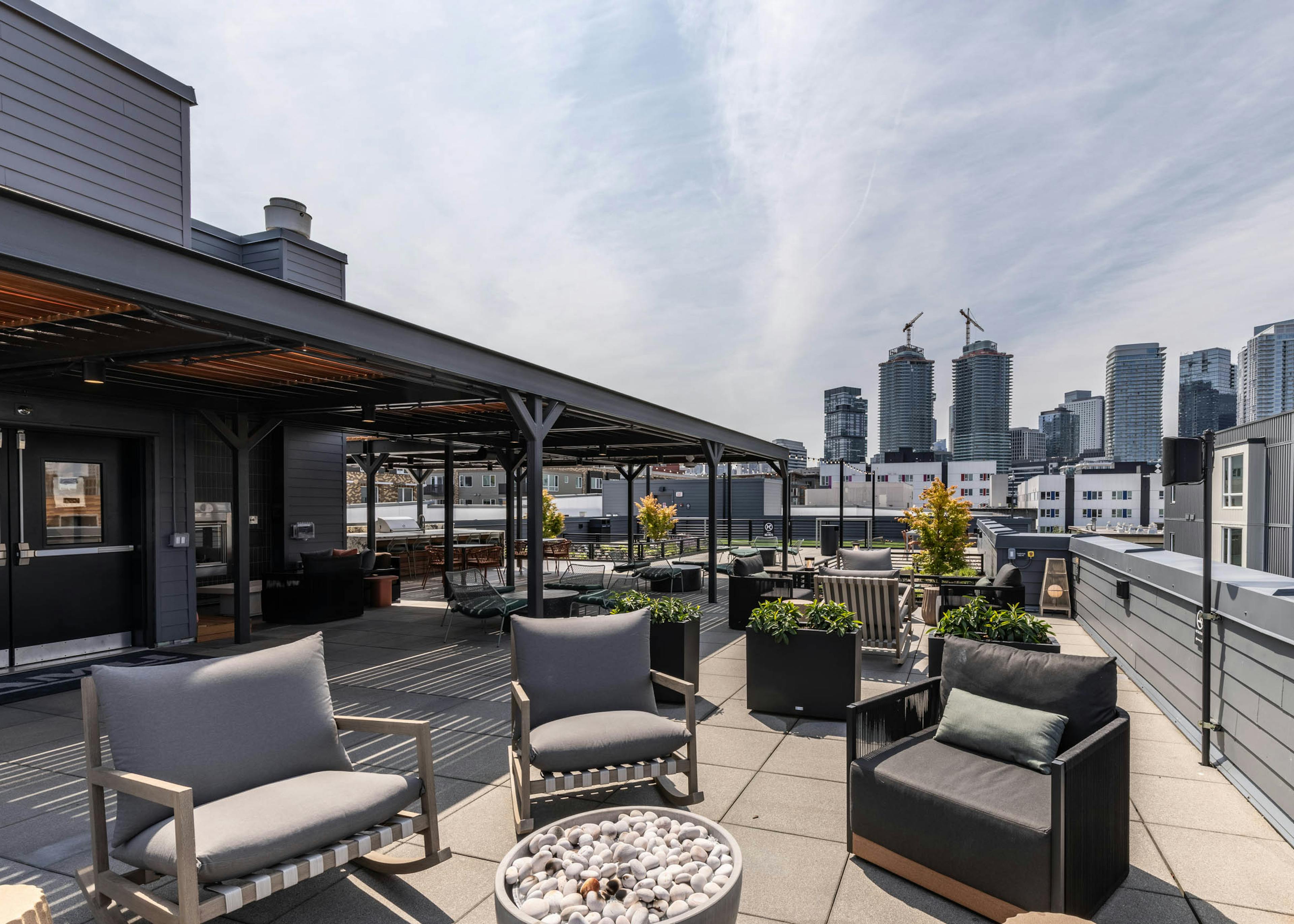 Rooftop lounge with cushioned chairs, fire pit, skyline views, and covered seating under black pergola at AMLI 535 apartments.