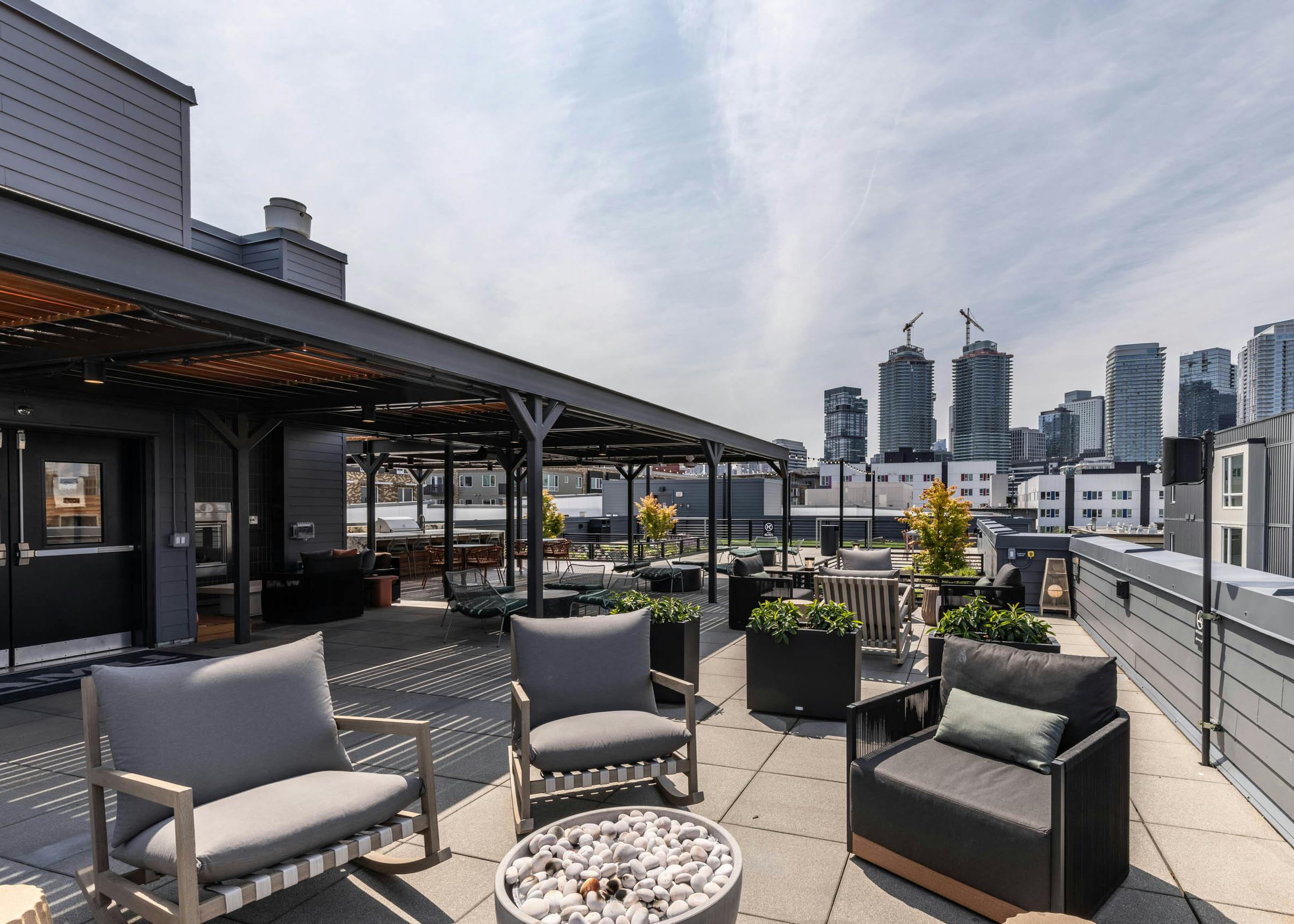 Rooftop lounge with cushioned chairs, fire pit, skyline views, and covered seating under black pergola at AMLI 535 apartments.
