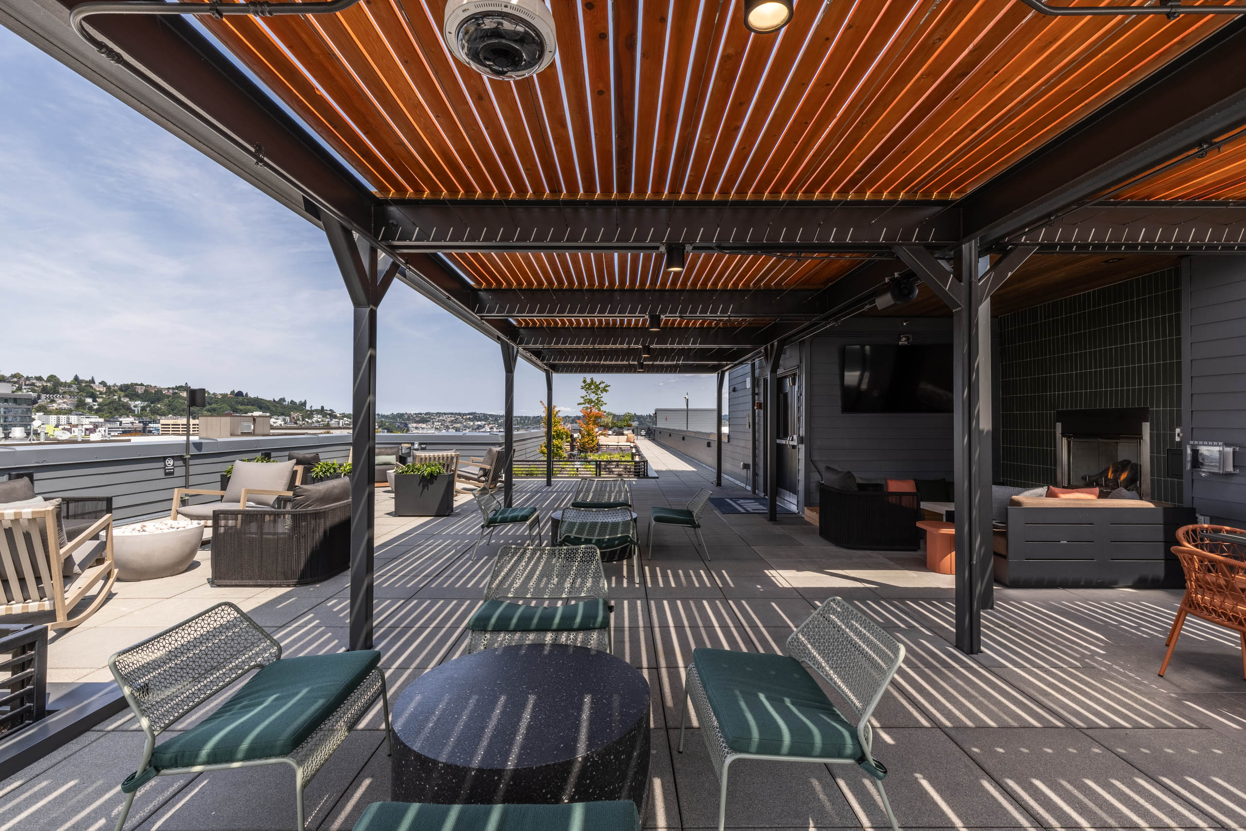 Shaded rooftop terrace at AMLI 535 with white chairs with green cushions, lounge furniture, and cityscape views under wood-slat canopy.