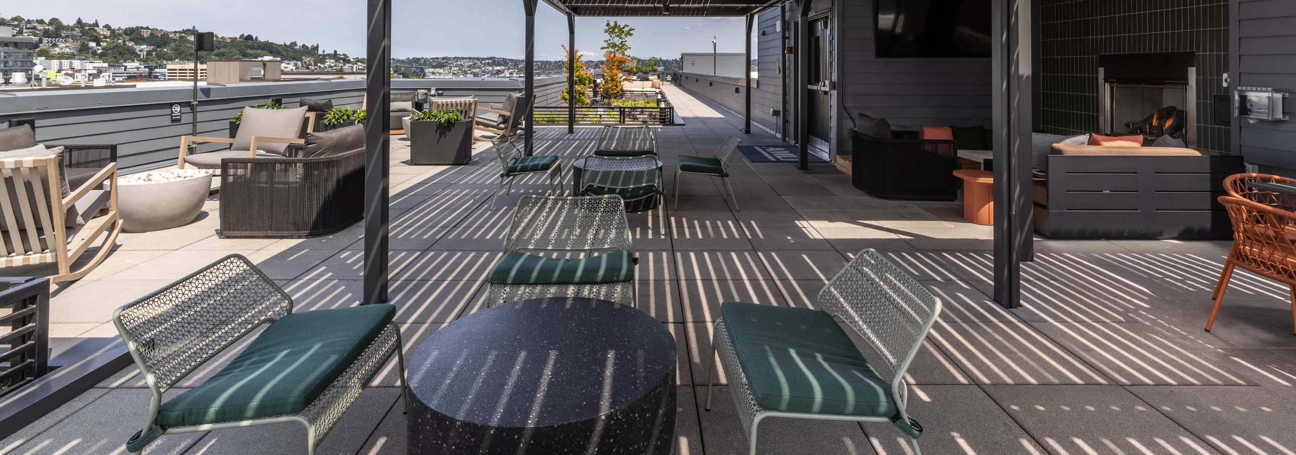 Shaded rooftop terrace at AMLI 535 with white chairs with green cushions, lounge furniture, and cityscape views under wood-slat canopy.