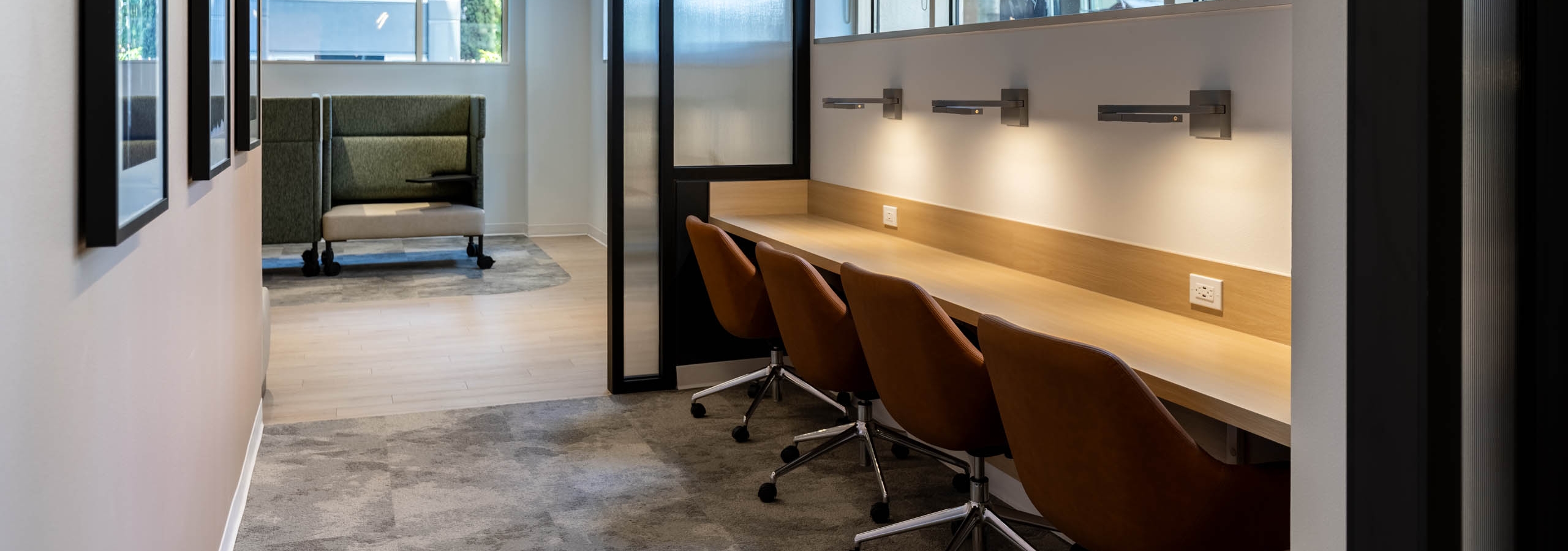 Interior workspace at AMLI 535 apartments featuring long wooden desk with four leather chairs, mounted lights, and large windows.
