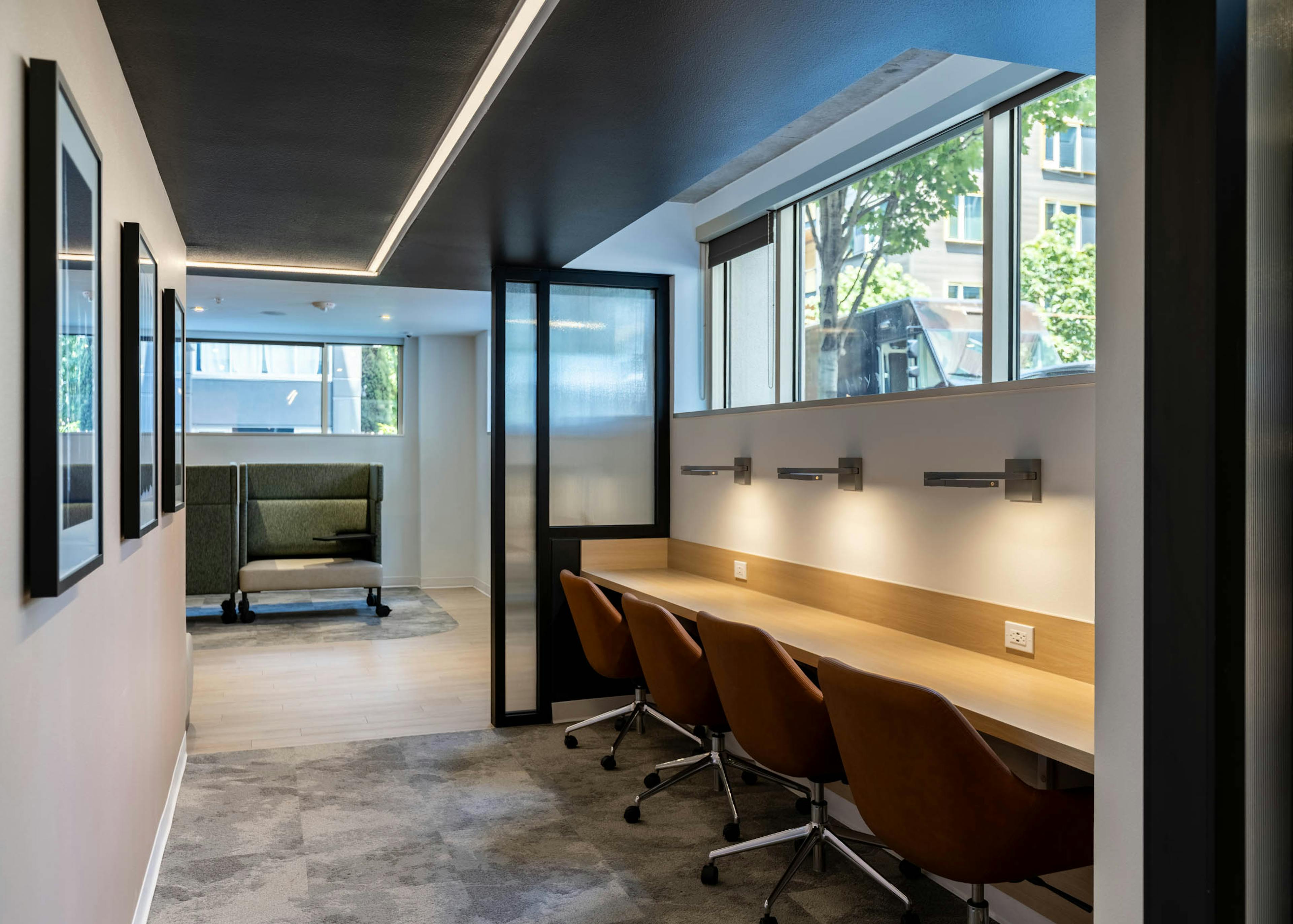 Interior workspace at AMLI 535 apartments featuring long wooden desk with four leather chairs, mounted lights, and large windows.