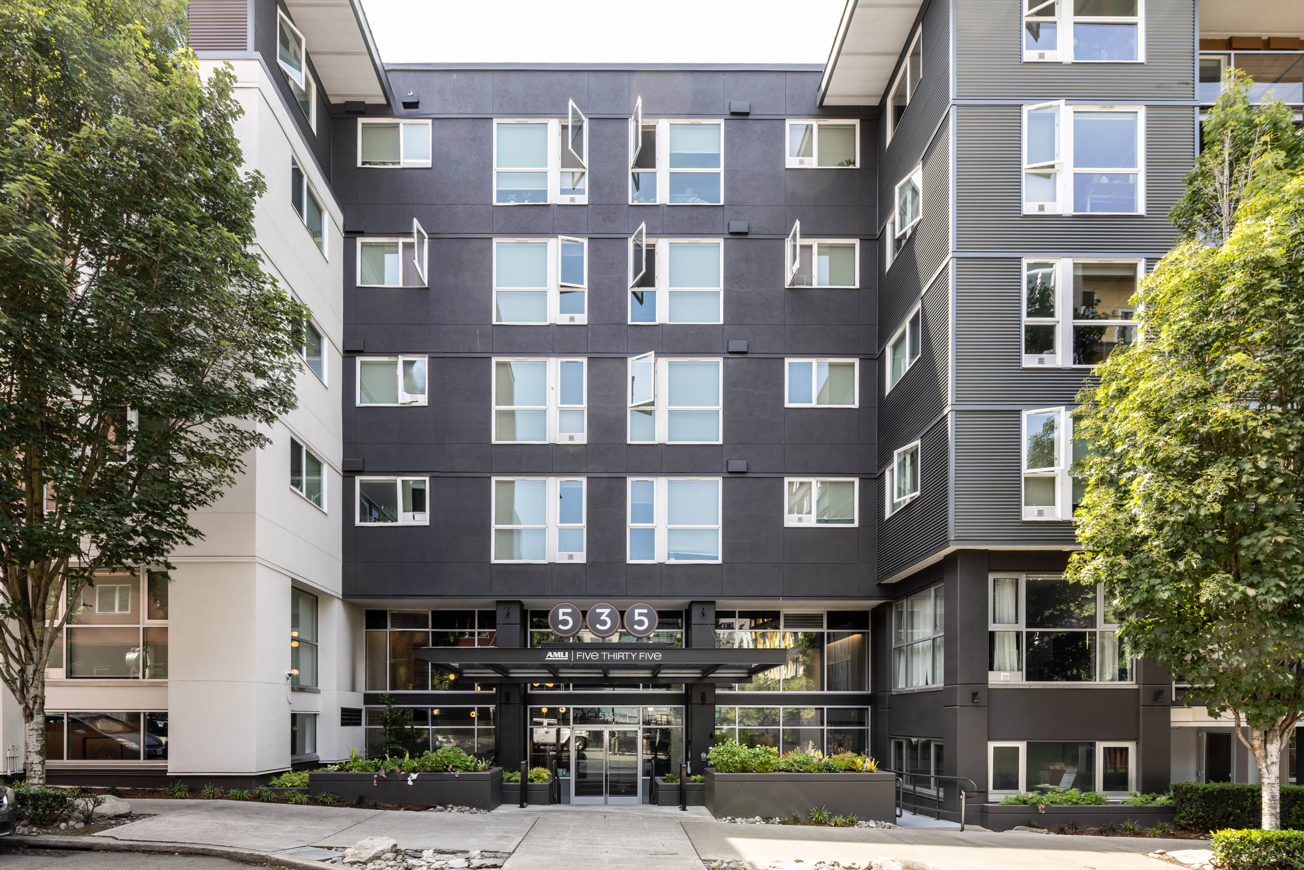 Full exterior view of AMLI 535 apartments showing modern black and white façade, open windows, entry glass canopy, and landscaping.