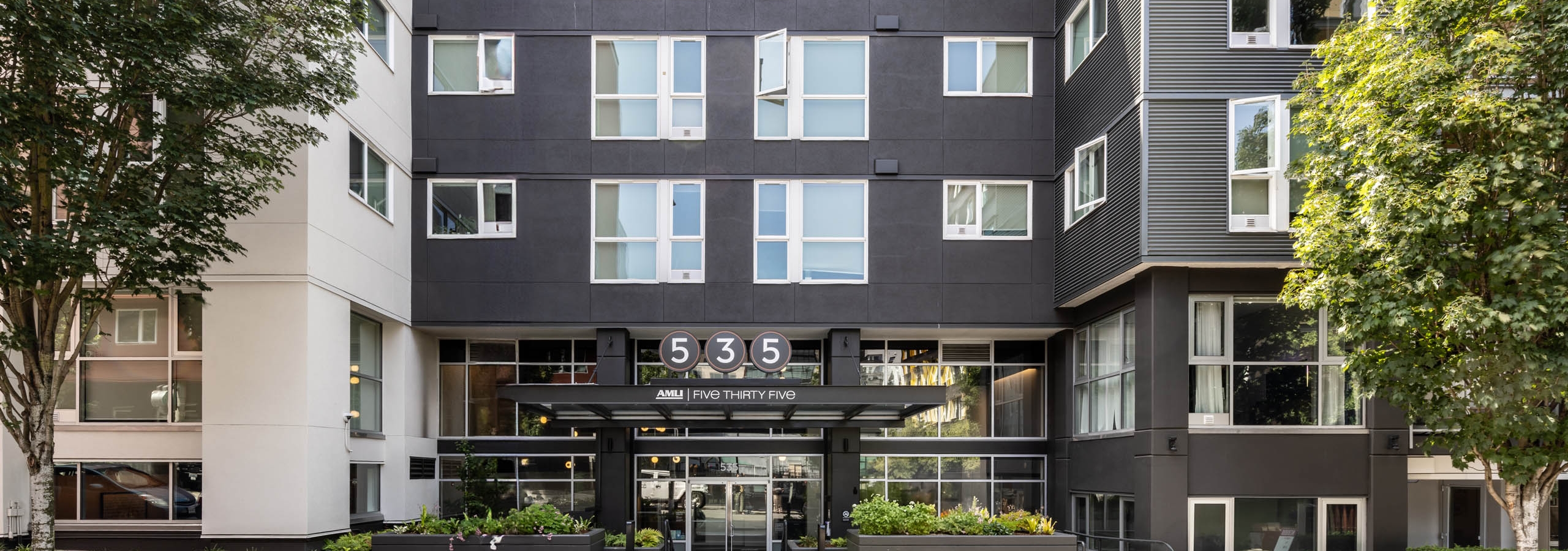 Full exterior view of AMLI 535 apartments showing modern black and white façade, open windows, entry glass canopy, and landscaping.