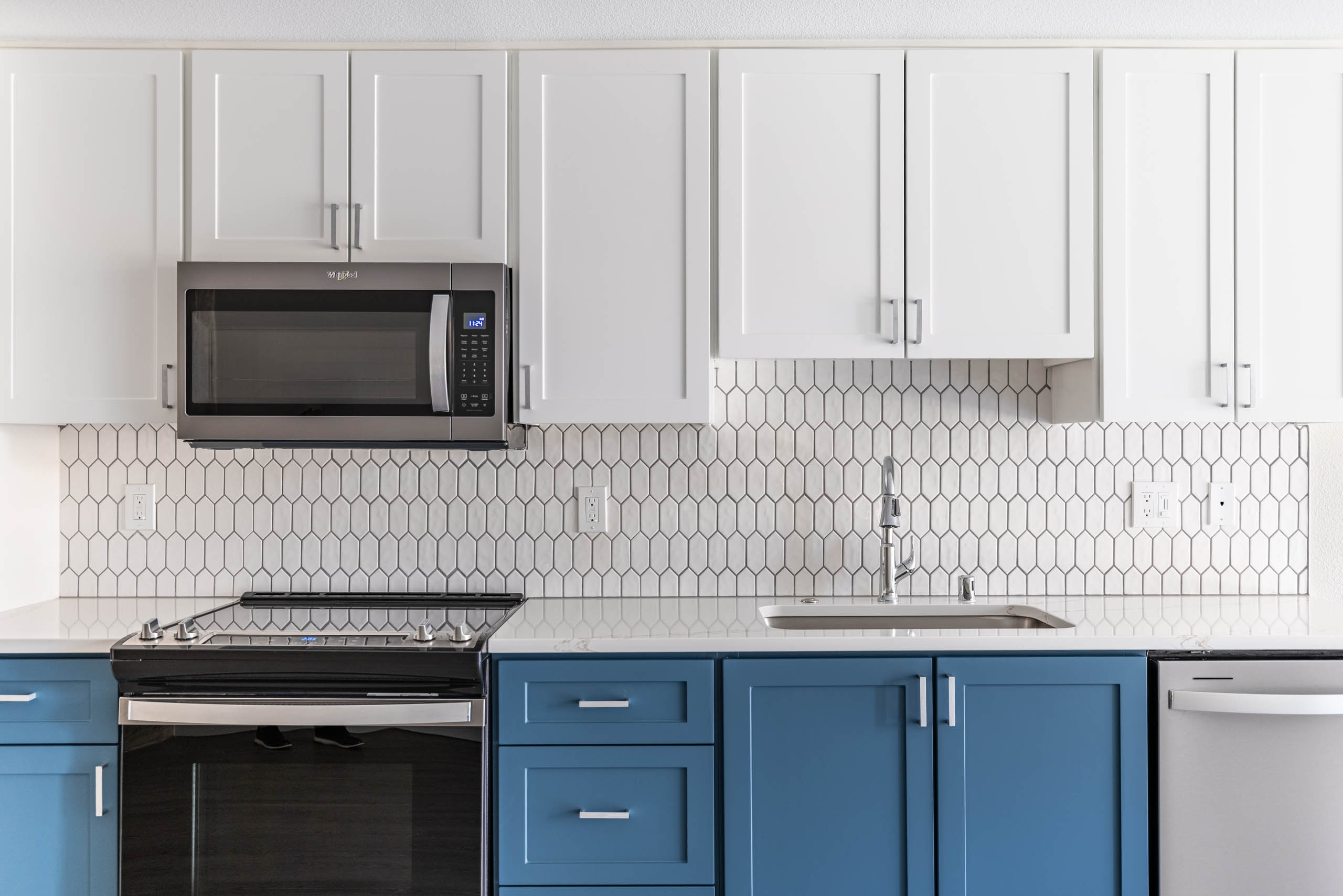 Kitchen at AMLI 535 apartments with white upper cabinets, blue lower cabinets, hex tile backsplash and stainless appliances.