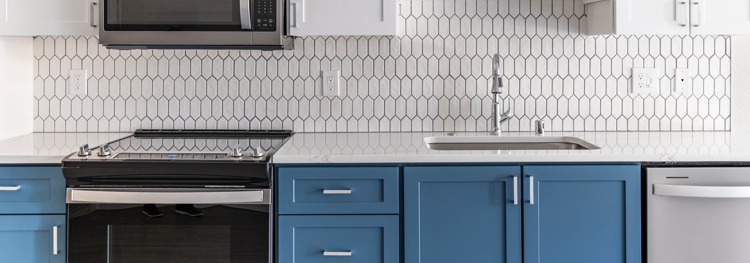 Kitchen at AMLI 535 apartments with white upper cabinets, blue lower cabinets, hex tile backsplash and stainless appliances.