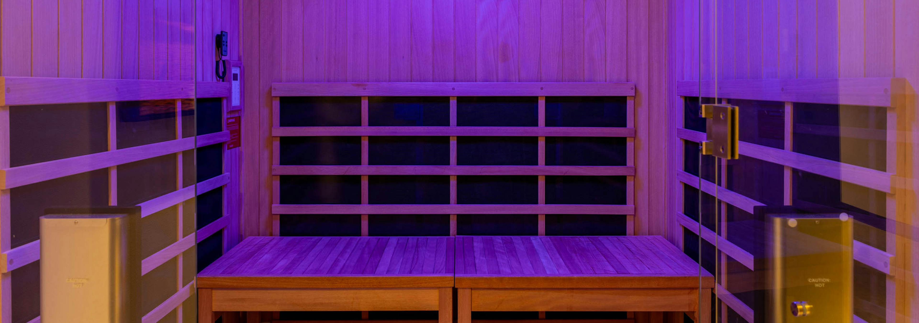 Infrared sauna room at AMLI 535 apartments featuring natural wood interior, bench seating, and soft purple mood lighting.