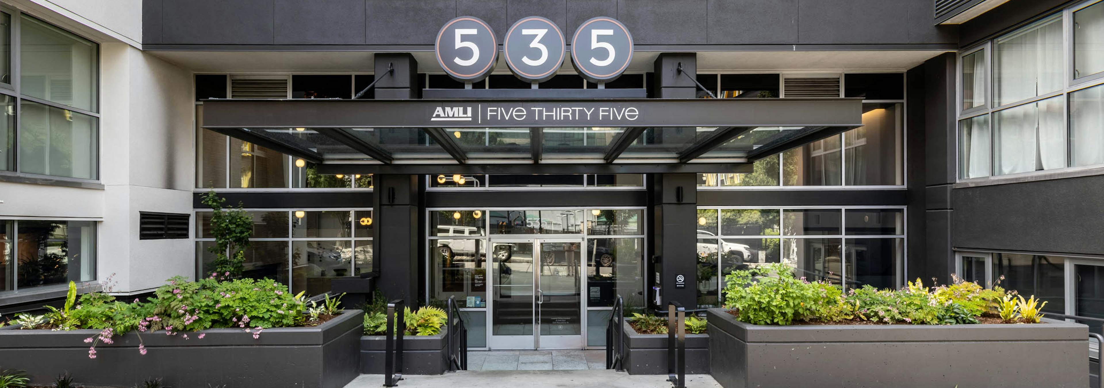 Exterior entrance of AMLI 535 apartments with black façade, glass canopy, planters, and large 535 sign above front doors.