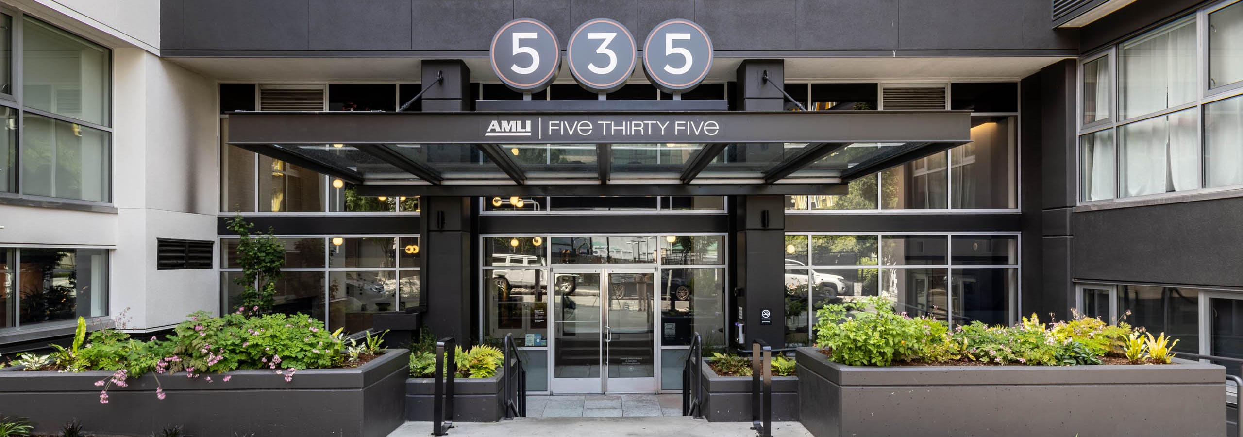 Exterior entrance of AMLI 535 apartments with black façade, glass canopy, planters, and large 535 sign above front doors.
