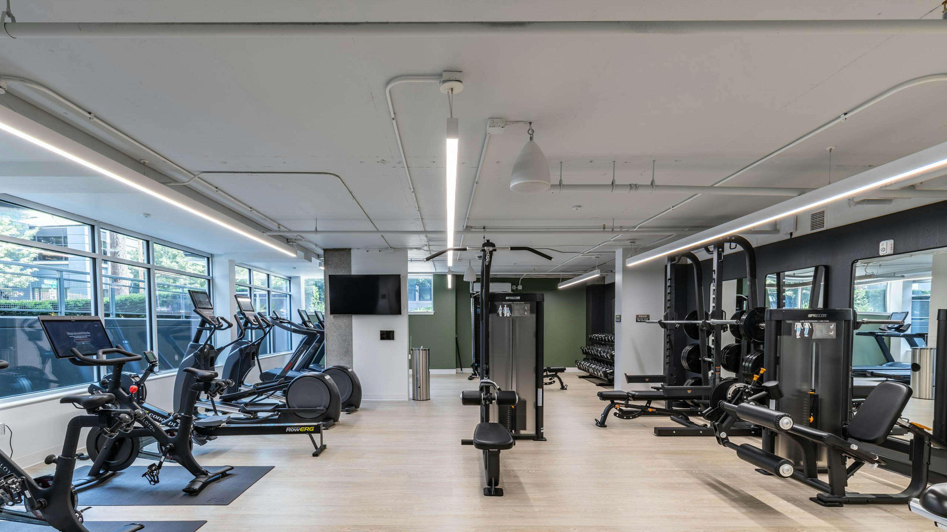 Full view of fitness center with cardio machines, strength equipment, free weights, and light wood-style flooring at AMLI 535 apartments.