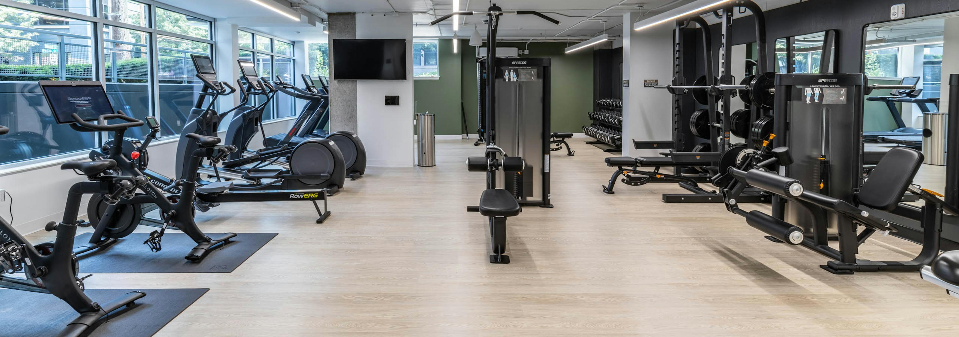 Full view of fitness center with cardio machines, strength equipment, free weights, and light wood-style flooring at AMLI 535 apartments.