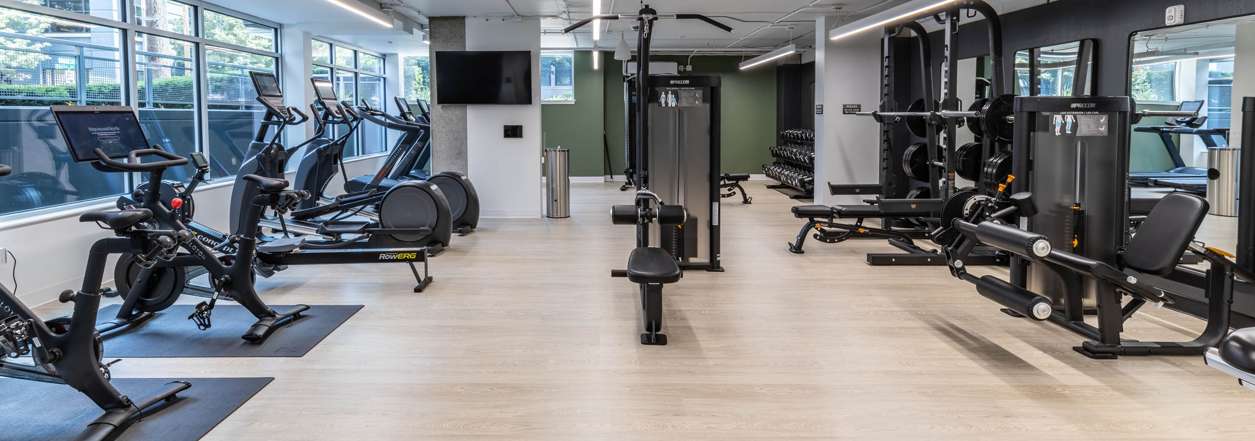 Full view of fitness center with cardio machines, strength equipment, free weights, and light wood-style flooring at AMLI 535 apartments.