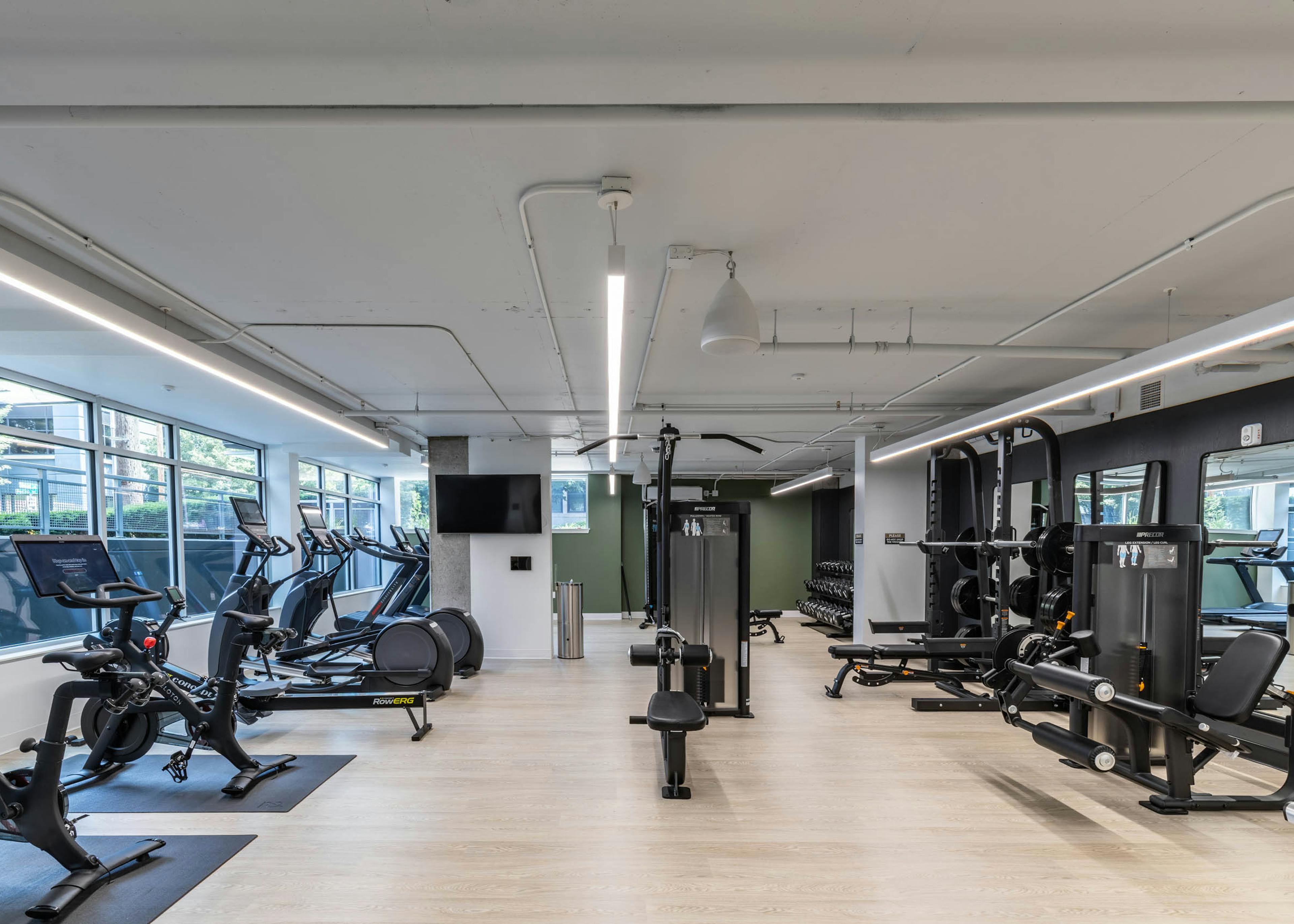Full view of fitness center with cardio machines, strength equipment, free weights, and light wood-style flooring at AMLI 535 apartments.
