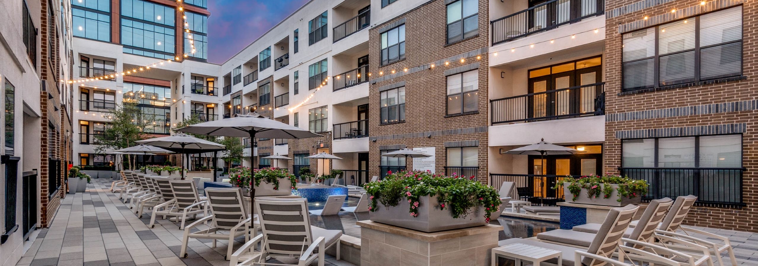 Dusk cooling spa at AMLI Quadrangle with loungers, umbrellas, potted plants and string lights with office building in the background.
