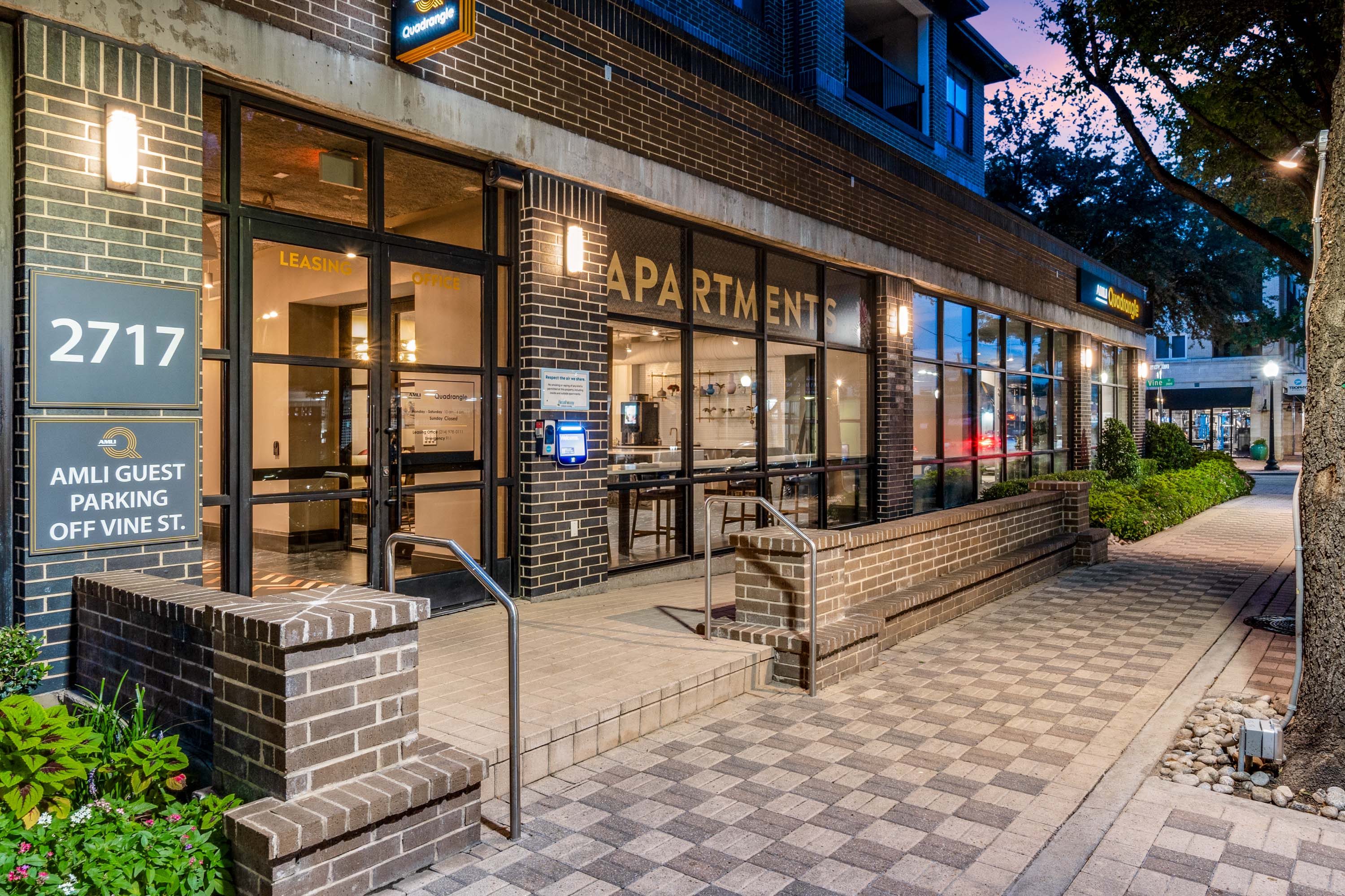 AMLI Quadrangle street entrance at night with checkered pavers and building address with glass windows and step with handrail.