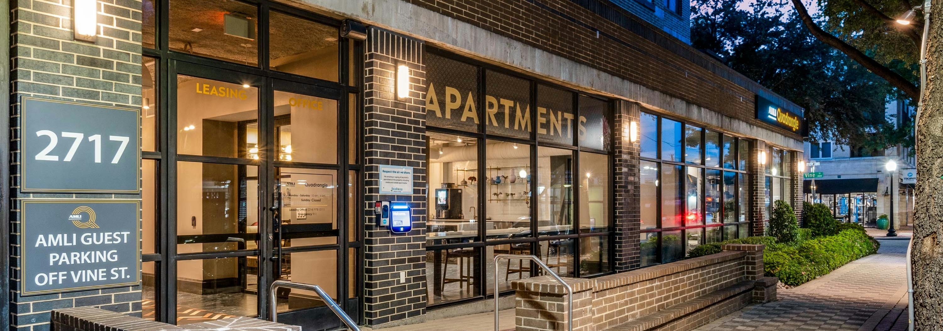 AMLI Quadrangle street entrance at night with checkered pavers and building address with glass windows and step with handrail.