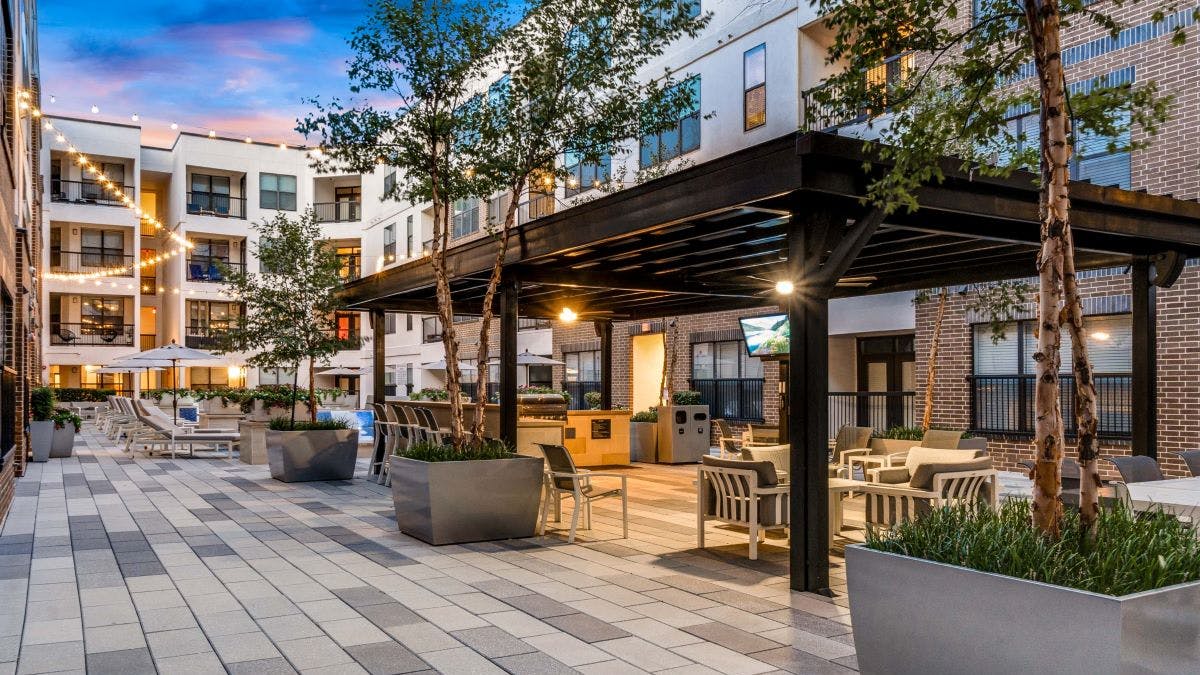AMLI Quadrangle covered barbeque grill and seating area with television and surrounding planted trees with string lights in the background.