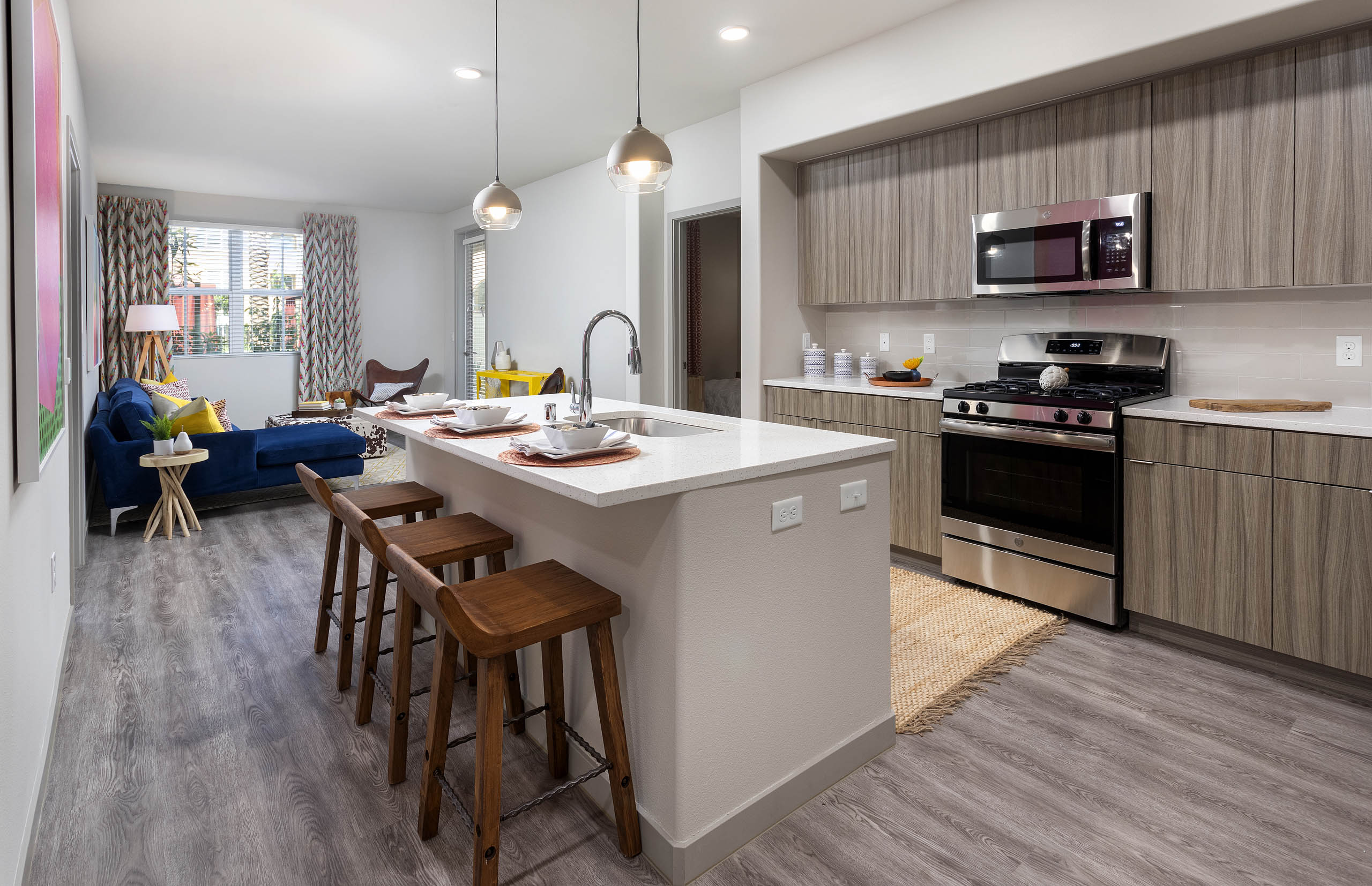 Open layout of AMLI Camarillo apartment kitchen with island, barstools and living area featuring a navy sofa and patterned drapes