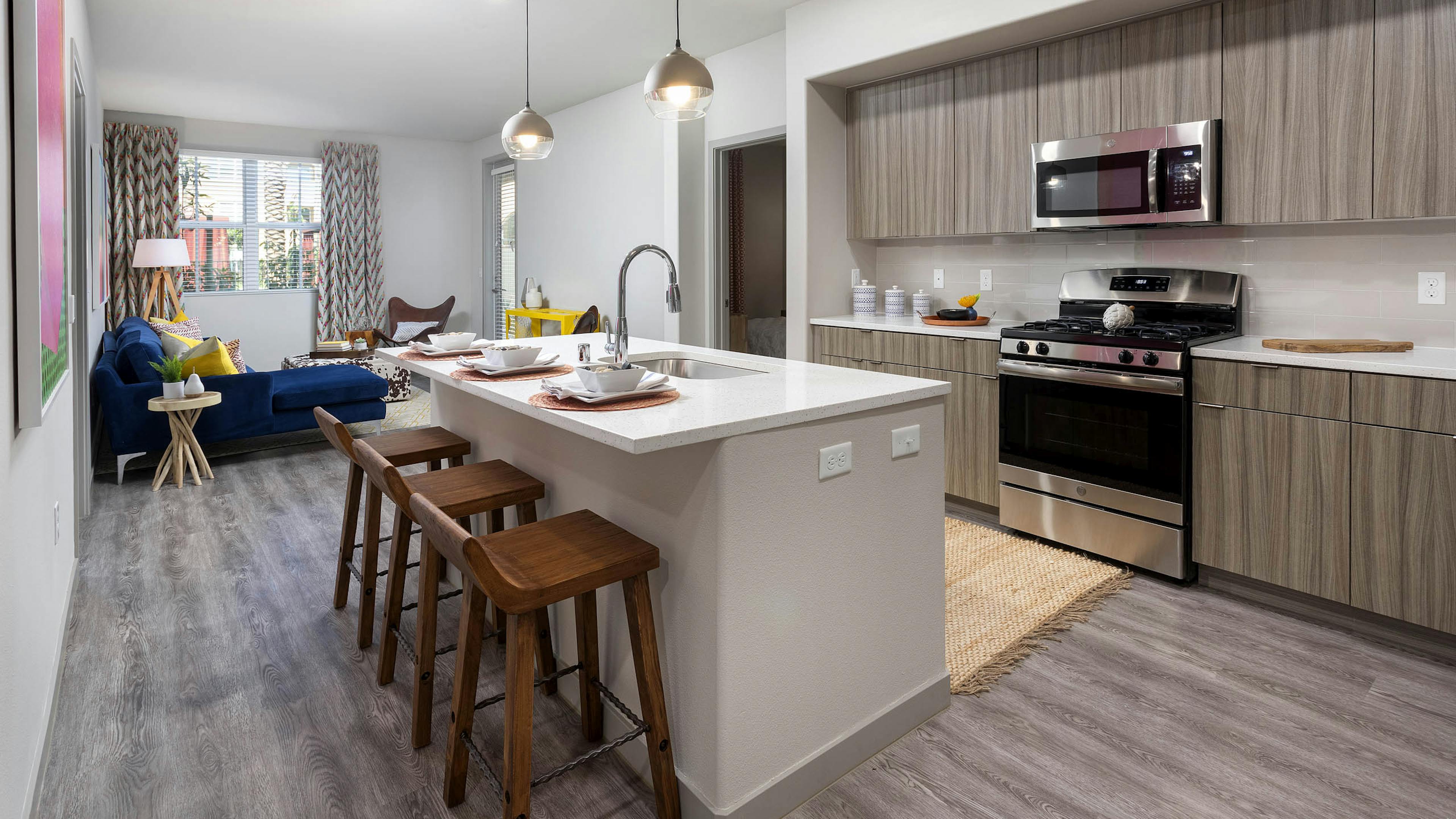 Open layout of AMLI Camarillo apartment kitchen with island, barstools and living area featuring a navy sofa and patterned drapes