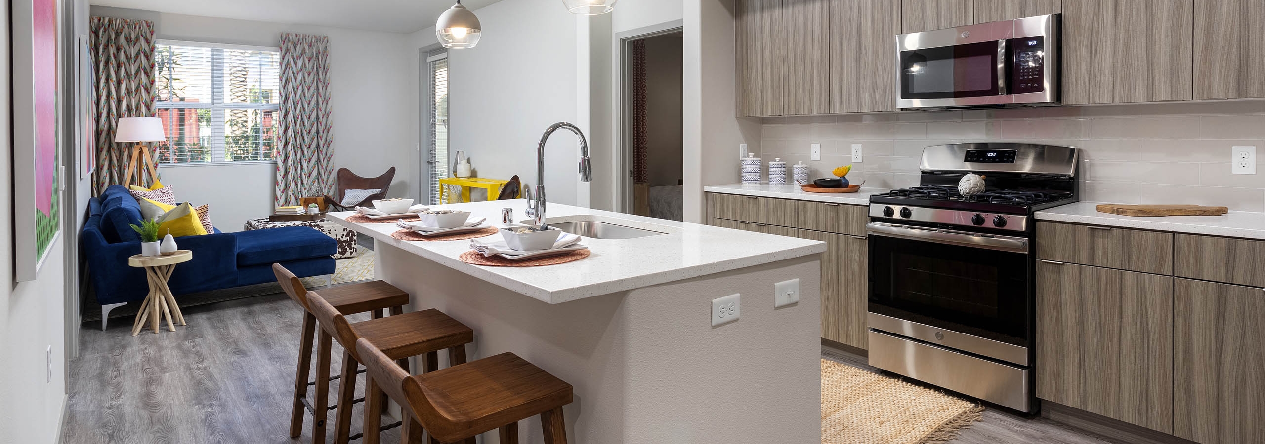 Open layout of AMLI Camarillo apartment kitchen with island, barstools and living area featuring a navy sofa and patterned drapes