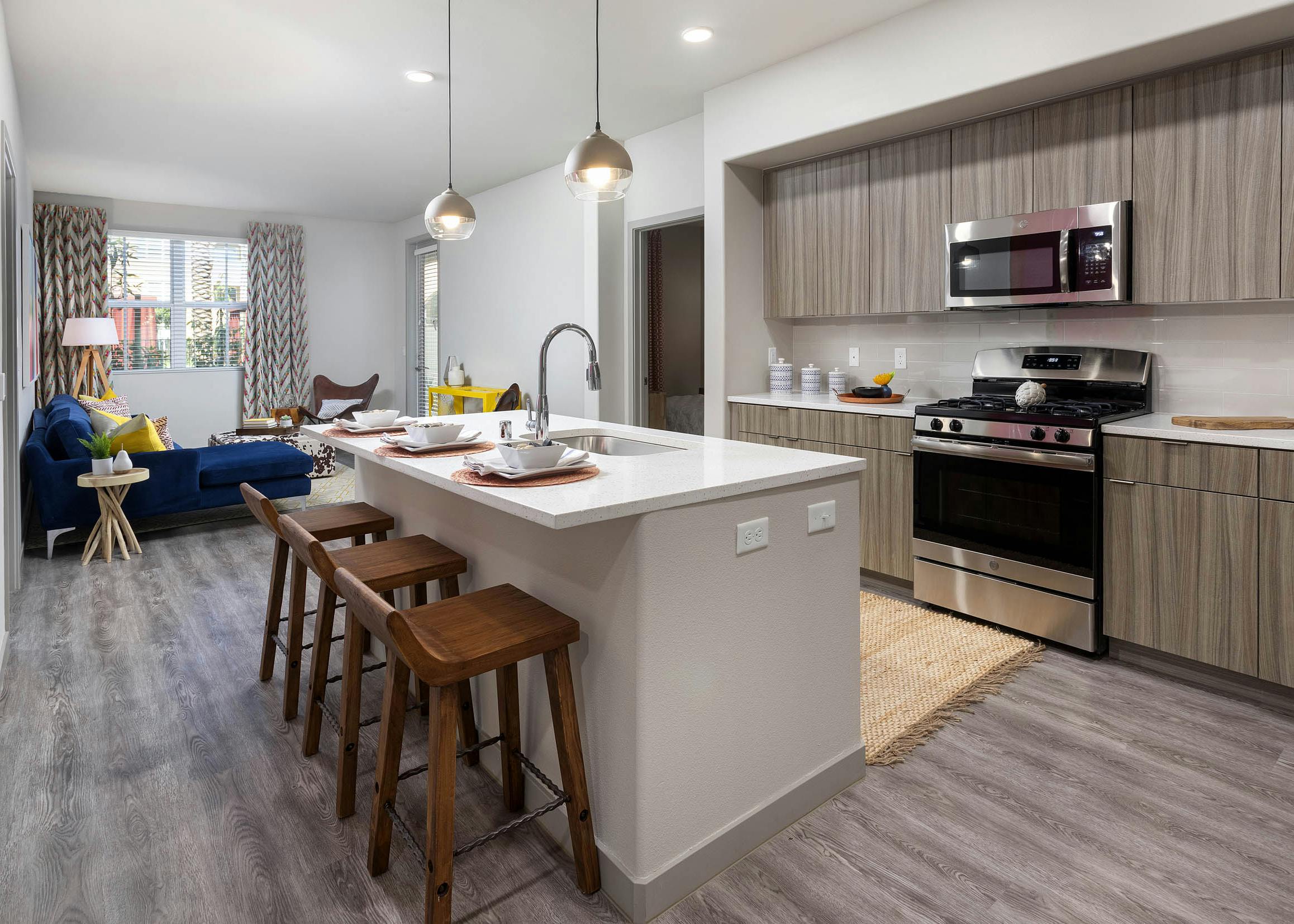 Open layout of AMLI Camarillo apartment kitchen with island, barstools and living area featuring a navy sofa and patterned drapes