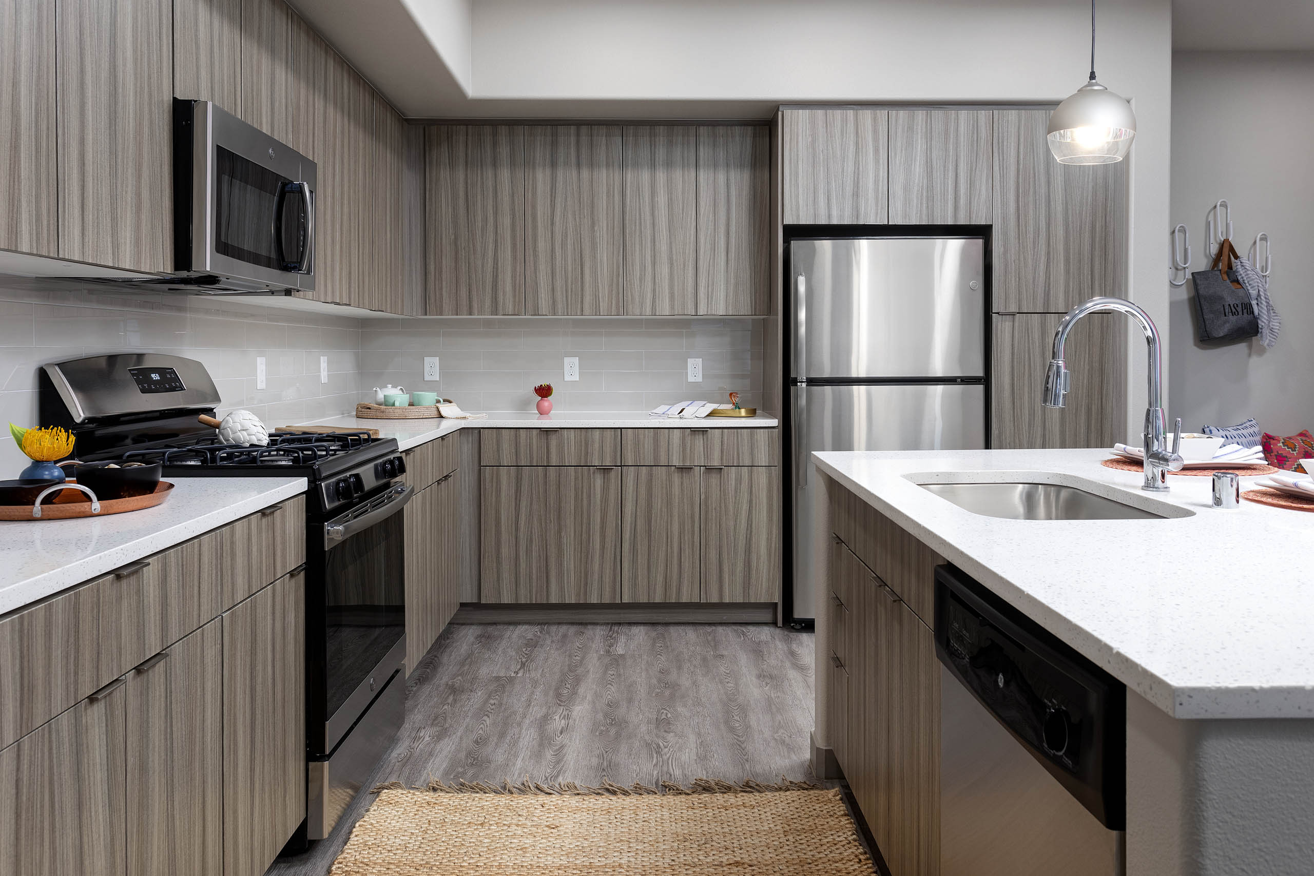 Interior view of AMLI Camarillo apartment kitchen with light wood grain cabinets, stainless appliances, quartz counters and tile backsplash