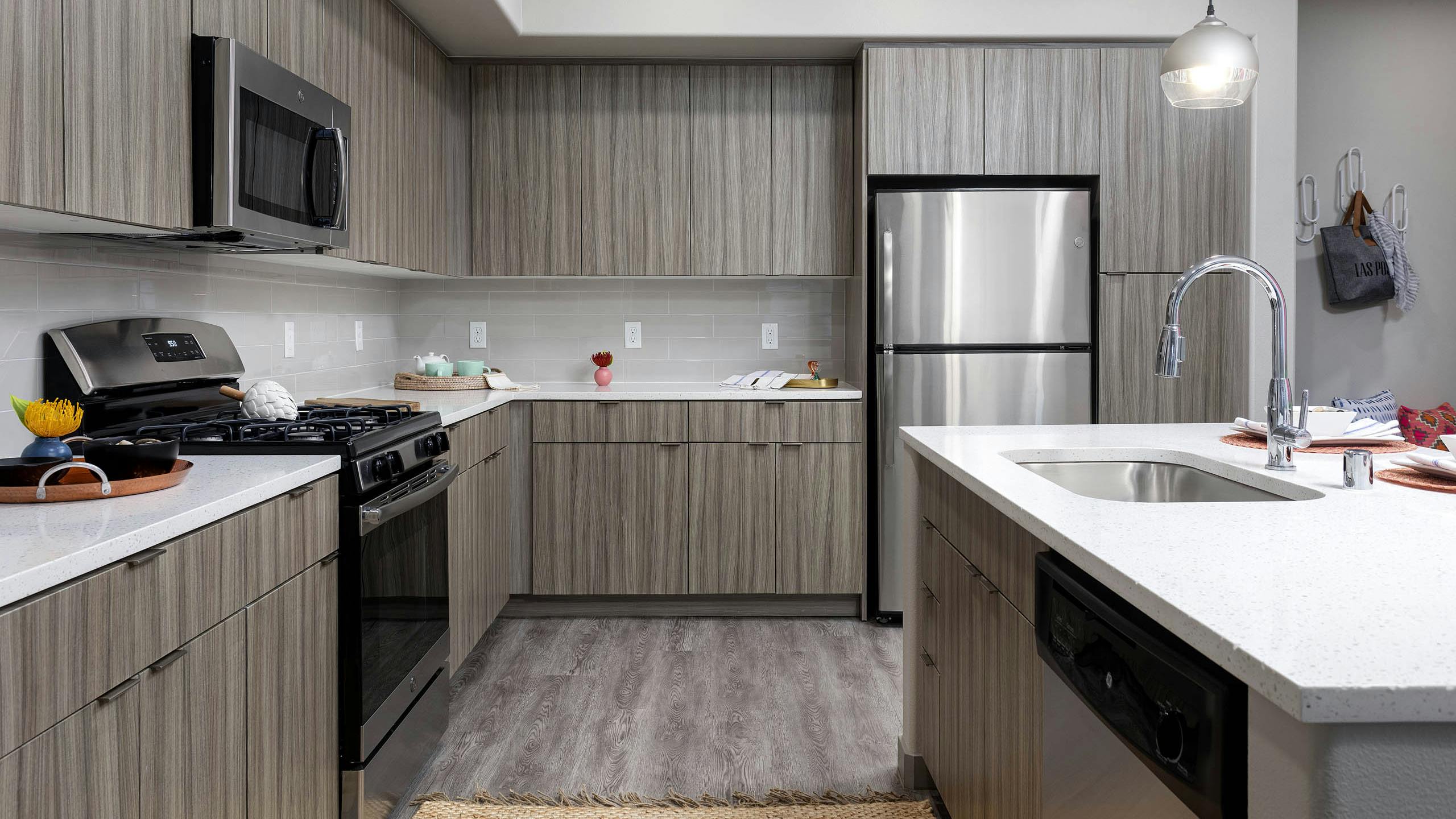 Interior view of AMLI Camarillo apartment kitchen with light wood grain cabinets, stainless appliances, quartz counters and tile backsplash
